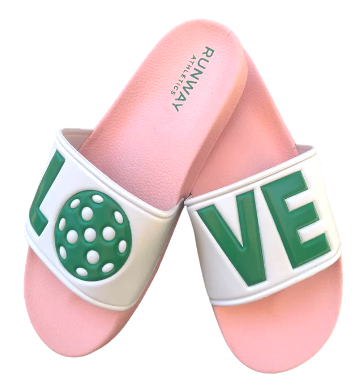 The Pickleball Slides - Pink, Green & White by Runway Athletics feature two pink slides with white bands spelling LOVE in green letters, where the "O" is a green pickleball. The insole is stamped RUNWAY ATHLETICS in green.
