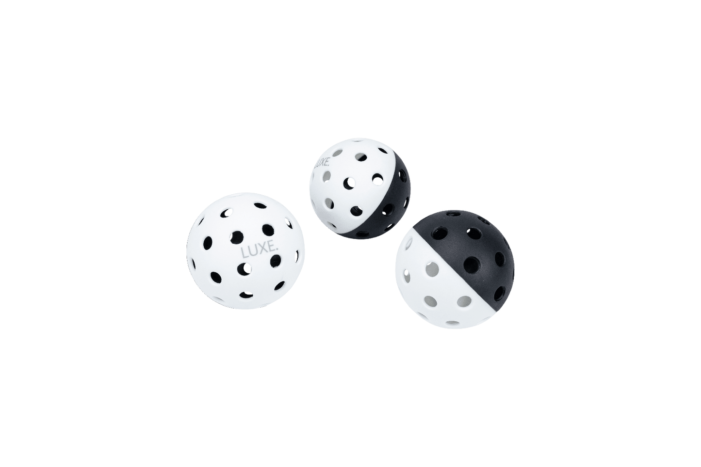 Three LUXE Pickleballs by LUXE Pickleball—with high-visibility designs (two mostly white, one half black/half white)—hover against a plain background. These durable balls have evenly spaced holes, ideal for indoor and outdoor play.