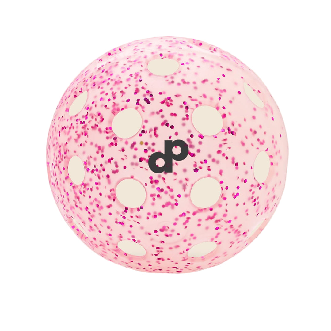 The Pink Glitter-Infused Pickleball Ball by Dope Pickleball Co. is light pink with circular holes, magenta speckles, and a black lowercase dp logo in the center, shown against a beige background with a soft shadow.