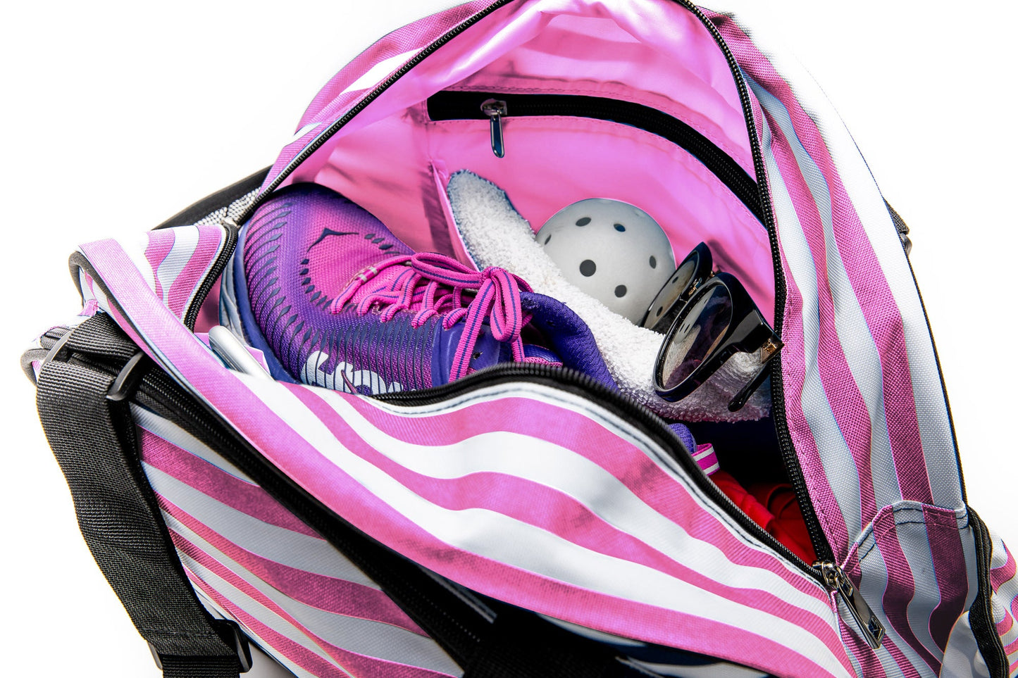The Stylish Stripe Pink Premium Women's Pickleball Bag by Pik'le'Ball Sports is open, showing a purple athletic shoe, white towel, black-and-white pickleball, and black sunglasses inside. Its light pink lining adds a stylish touch.