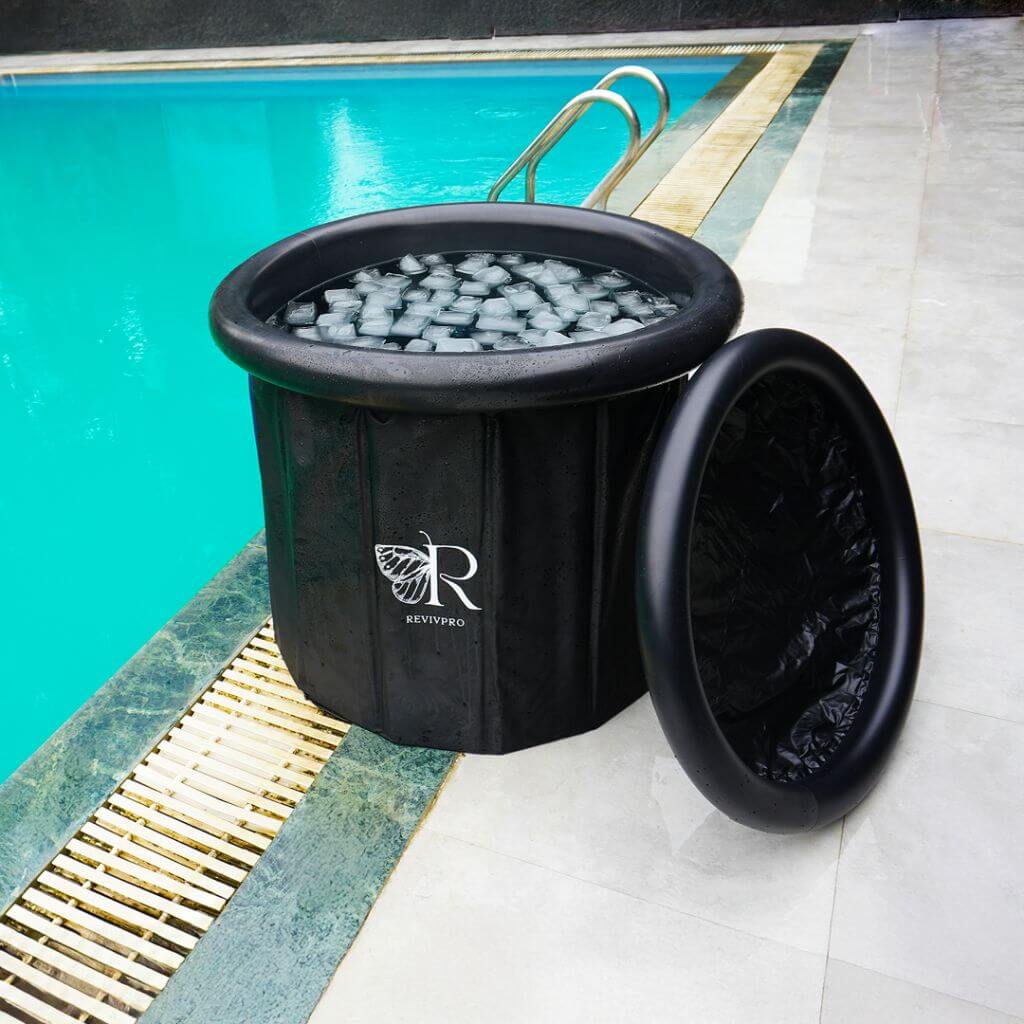 A black RevivPro Portable Foldable Ice Bath Tub, compatible with water chillers, filled with ice and water for cold therapy, sits by a pool. It displays a white leaf logo and includes a lid resting on the tiled edge.