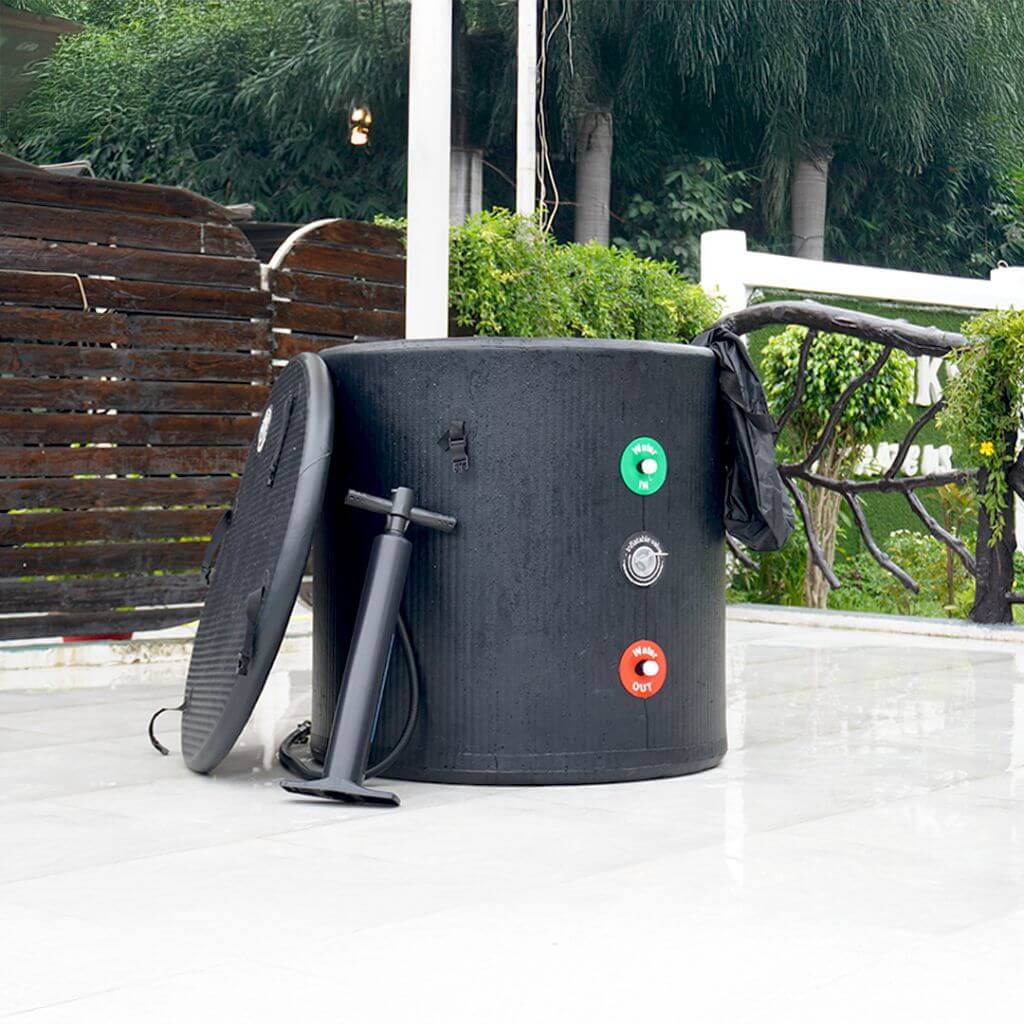 The RevivPro Portable Ice Bath Tub Pro, compatible with water chillers, stands outdoors on tiles near greenery. It features green, red, and white valve controls, a round lid nearby, and a black hand pump for cold plunge therapy.