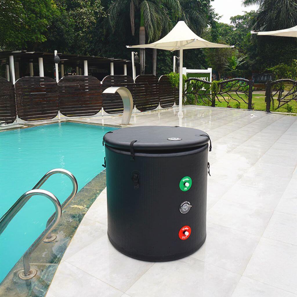 The RevivPro Portable Ice Bath Tub Pro, a large round black cold plunge with handles and green/red buttons, is placed on a white tiled poolside patio near a swimming pool, with lush trees, a wooden fence, and white canopies in the background.
