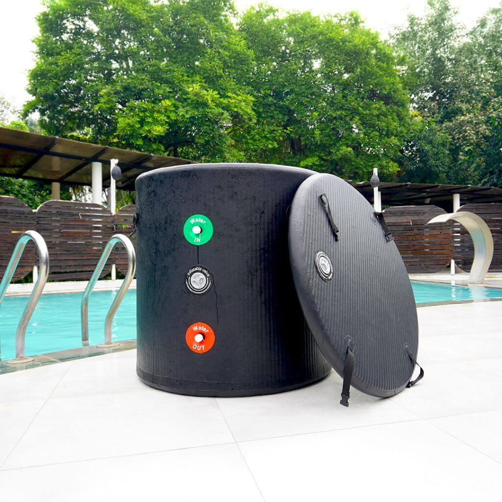 The RevivPro Portable Ice Bath Tub Pro, a black cylindrical recovery tub with a textured finish, carry straps, and colored water valves, stands poolside with trees and a swimming pool in the background. Water chiller compatible for easy cold therapy.