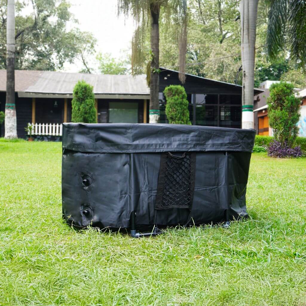 The RevivPro Portable Oval Ice Bath Tub X with Extra Length sits on green grass in a yard, featuring a mesh side pocket. This water chiller compatible cold plunge tub is ideal for outdoor use, with trees and a house visible in the background.