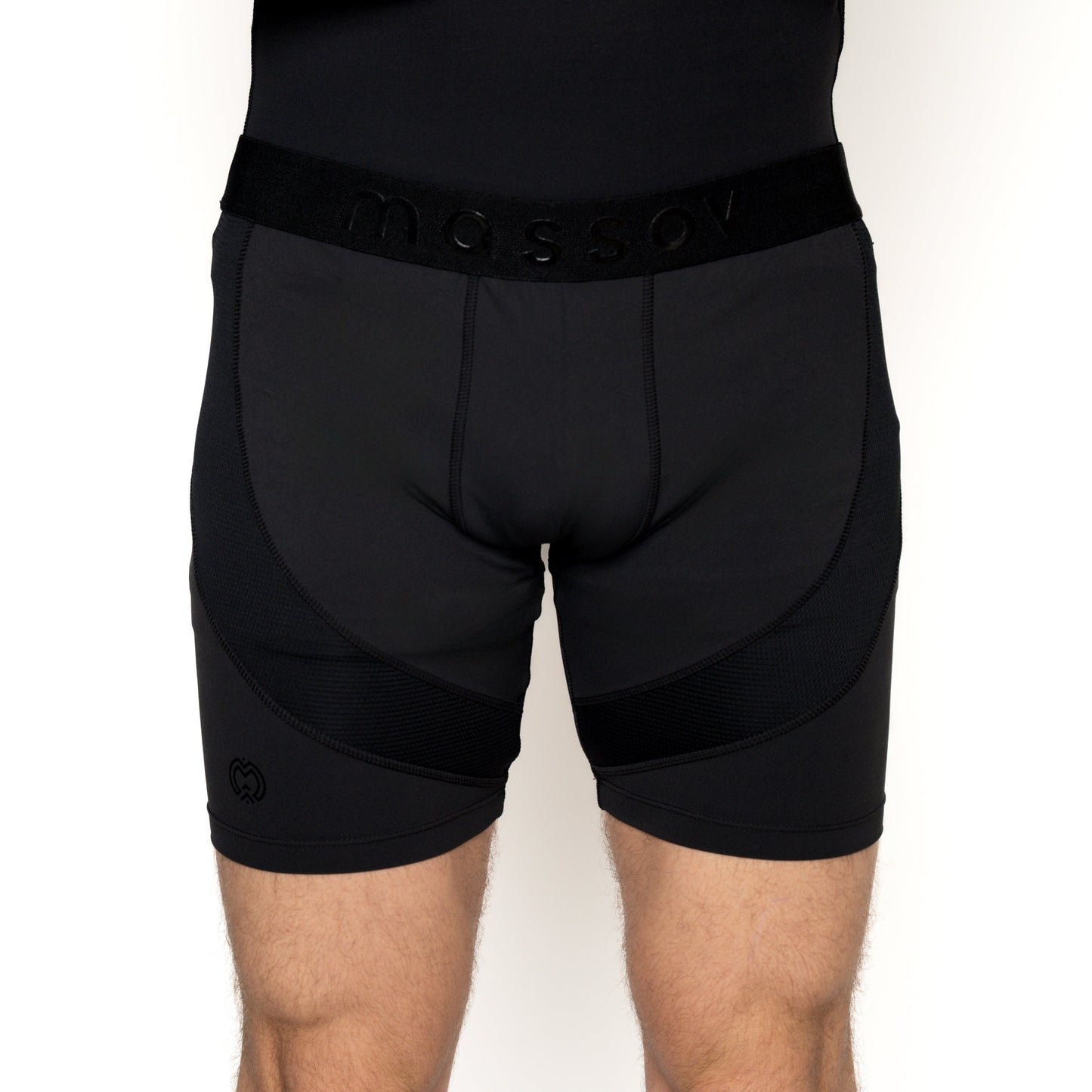 A boy wears Massov ProForm® Boys' 7" Compression Shorts in black, featuring a wide branded waistband, side mesh panels, and a small logo on the lower left leg. The shorts provide both style and comfort; upper body mostly out of frame.