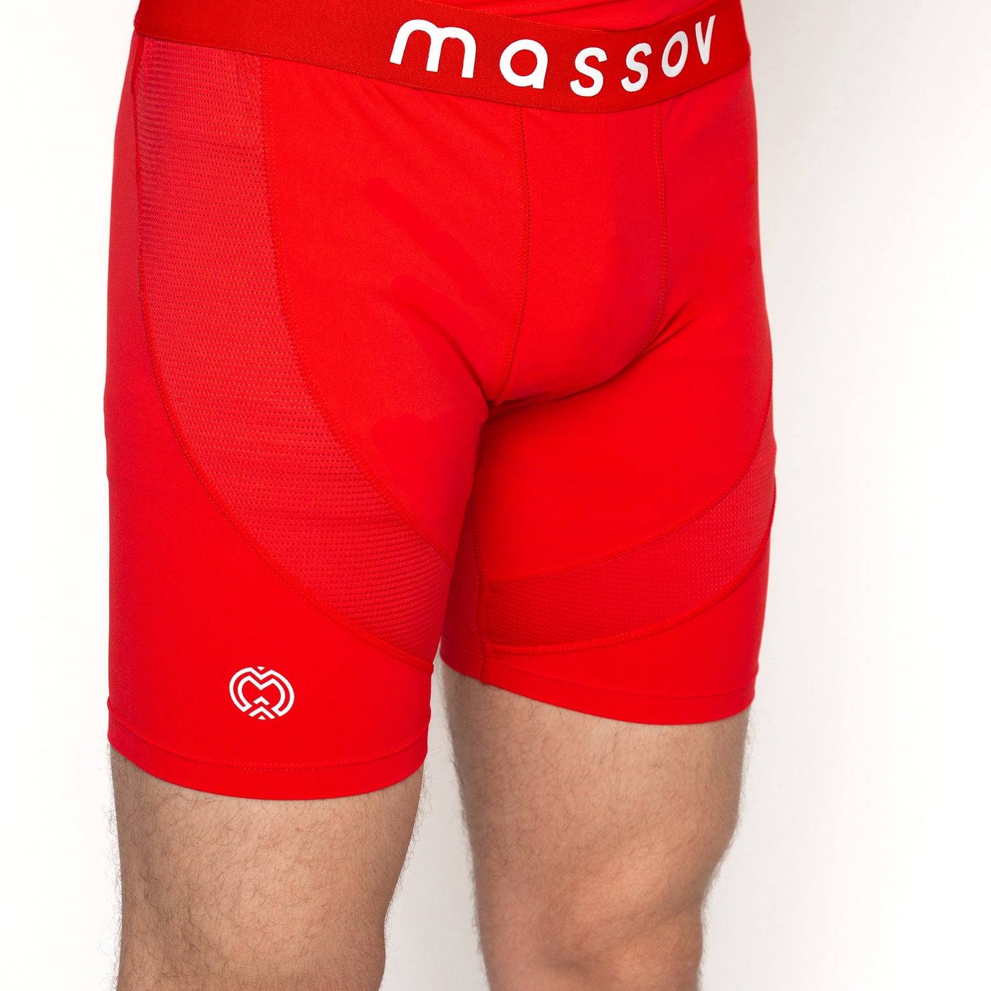 A boy is shown from the waist down wearing bright red Massov ProForm® Boys' 7″ Compression Shorts featuring mesh panels, a small white heart logo on the left thigh, and a branded waistband, against a plain white background.