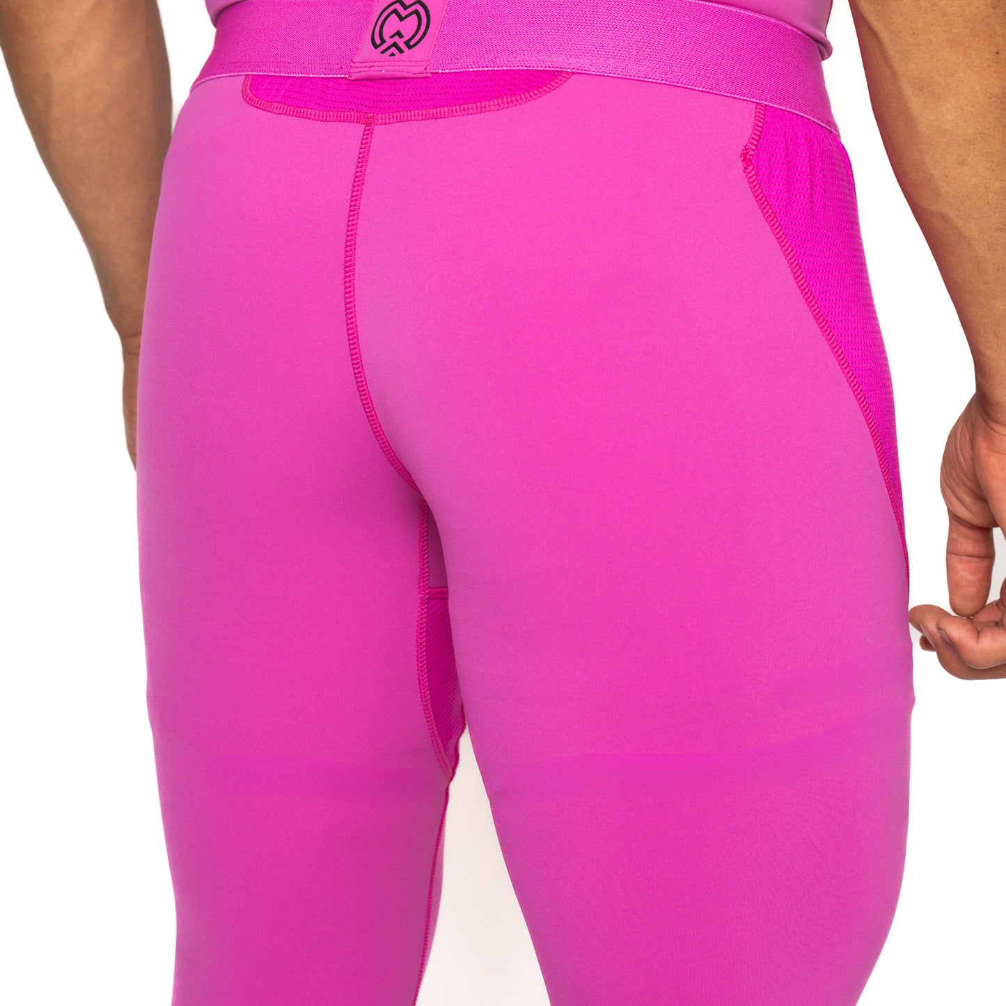 Close-up of a person wearing Massov ProForm® Boys' Compression Pants in bright pink, showing visible stitching and a small logo on the waistband. Only the lower back, upper legs, and part of a hand are visible against a white background.