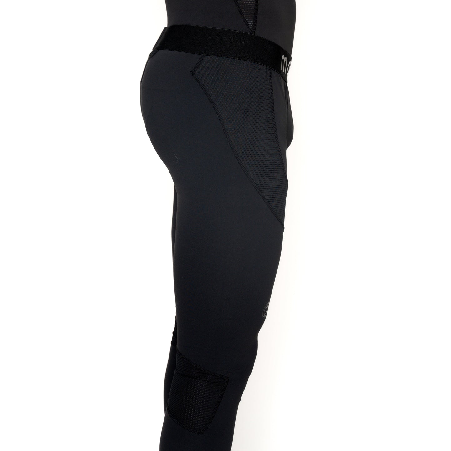 A person is shown from the side wearing fitted black Massov ProForm® Boys' Compression Pants with mesh panel details and a visible waistband, photographed against a white background. Only the lower torso and upper legs are visible.