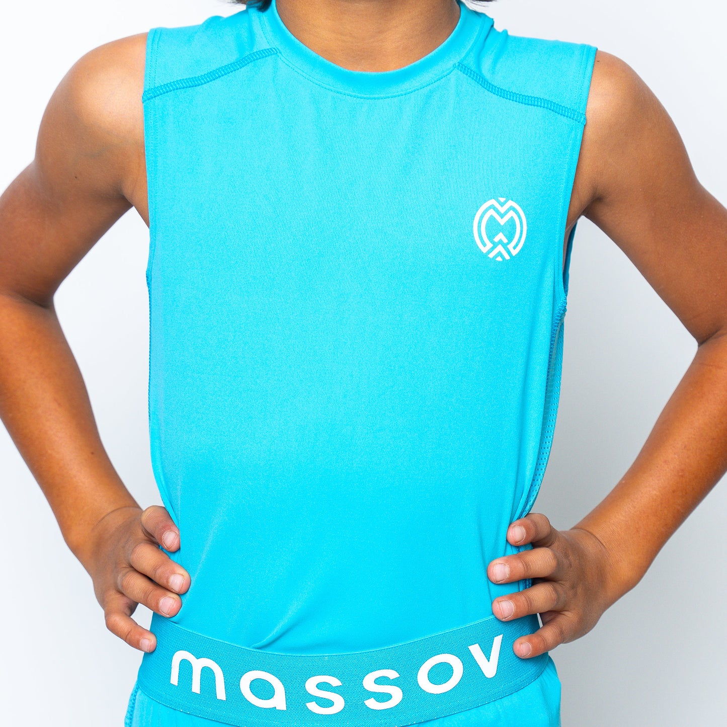 A person stands with hands on hips, wearing the Massov ProForm® Boys' Compression Tank Top, a sleeveless bright blue athletic shirt with a white left-chest logo and “massov” on the waistband. The plain white background highlights the outfit.