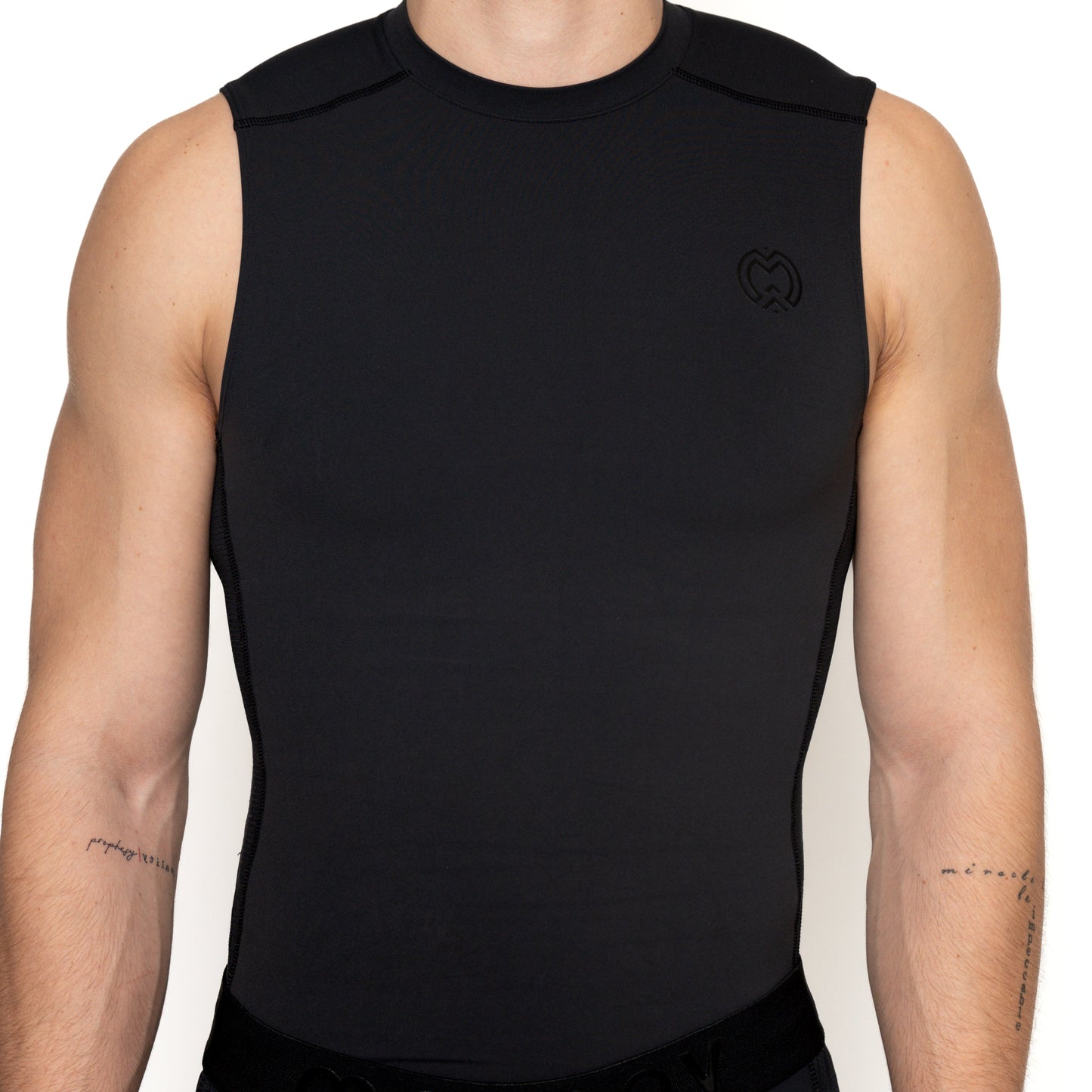 A person wears a Massov ProForm® Boys' Compression Tank Top, fitted and sleeveless, made from ProForm fabric. The shot focuses on the torso and tattooed upper arms, showing a small black emblem on the left chest against a plain background.