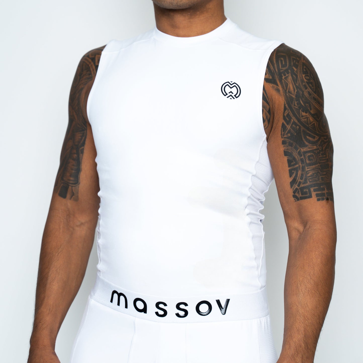 A person wears the Massov ProForm® Boys' Compression Tank Top with a heart-shaped chest logo and white shorts featuring "massov" on the waistband; their arms display bold geometric tattoos.