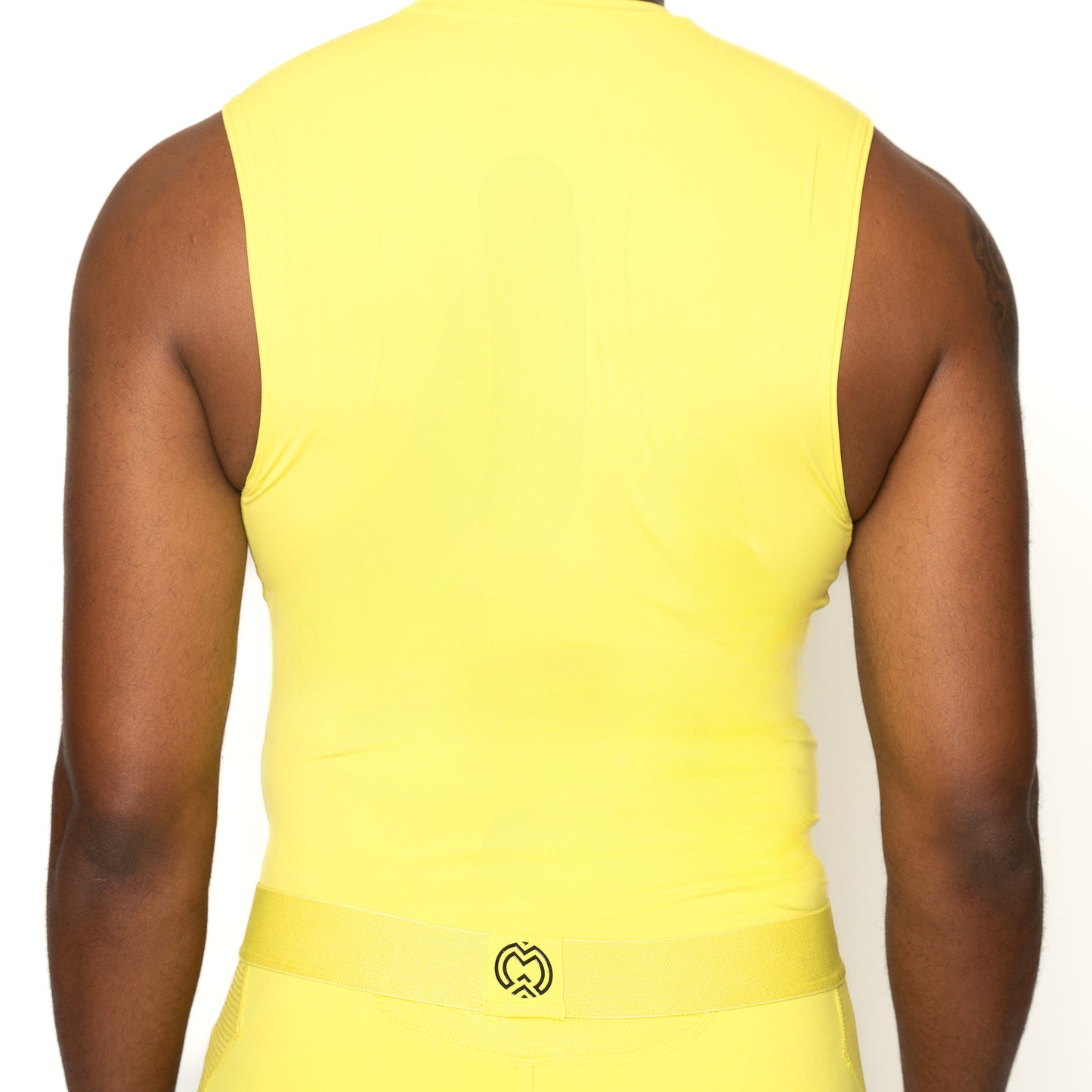 A person seen from behind wears a bright yellow Massov ProForm® Boys' Compression Tank Top and matching pants with a belt. The background is plain white, and a small black-and-yellow logo appears on the ProForm fabric at the waistband.