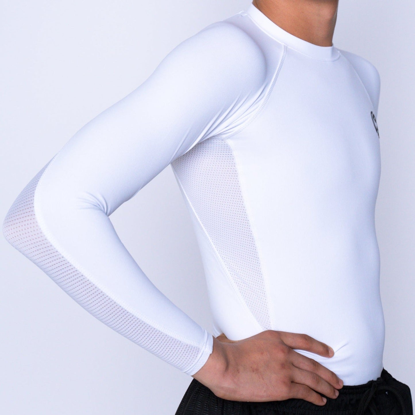A person wears a fitted Massov ProForm® Boys' Long Sleeve Compression Shirt in white, featuring mesh underarm panels. They stand with one hand on their hip against a plain white background, head partially out of frame.