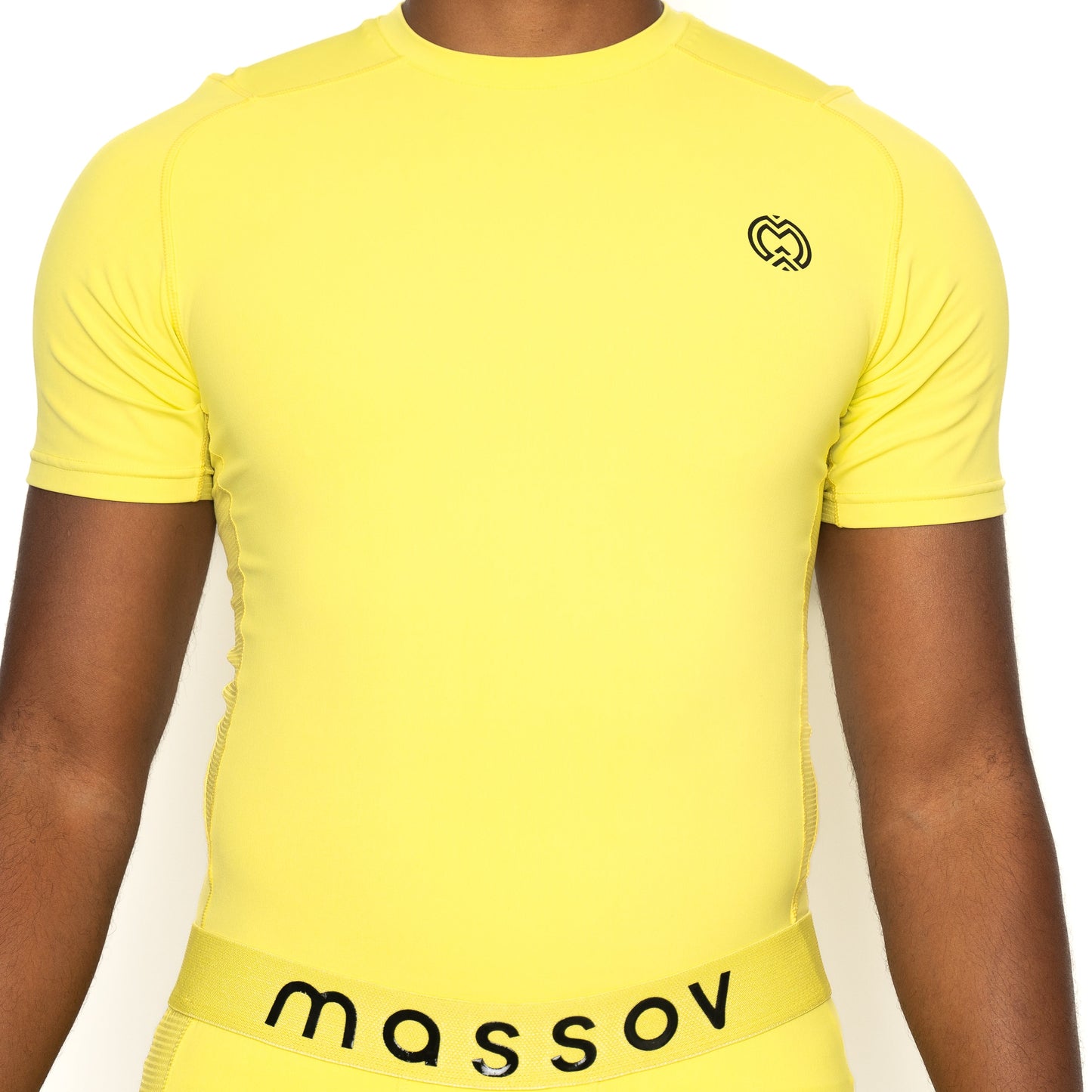 A boy wears the Massov ProForm® Boys' Short Sleeve Compression Shirt in yellow, featuring a small black logo on the left chest and a matching yellow waistband with “massov” in black. The background is plain white; his face is not visible.