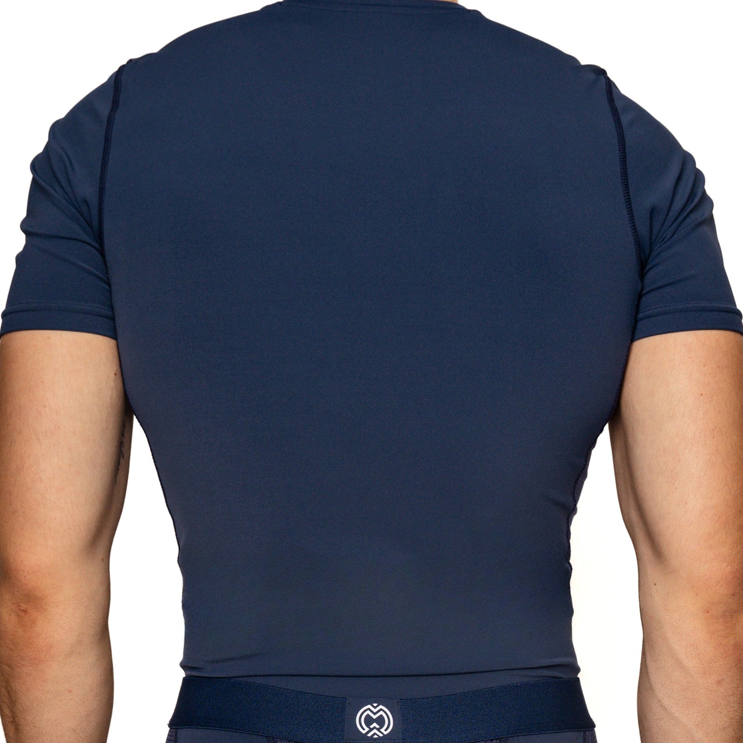 A boy with light skin is seen from the back wearing a Massov ProForm® Boys' Short Sleeve Compression Shirt in navy blue, featuring ProForm fabric, subtle seam lines, and a small white logo at the lower back.