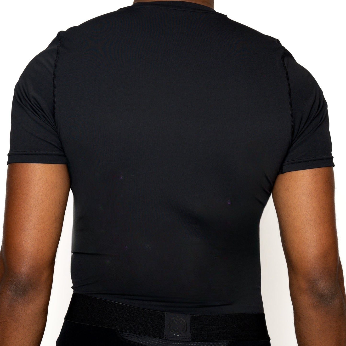 A boy is seen from the back wearing a Massov ProForm® Boys' Short Sleeve Compression Shirt. The fitted, stretchy shirt contours his torso as his arms rest at his sides. The upper body stands out against a plain white background.