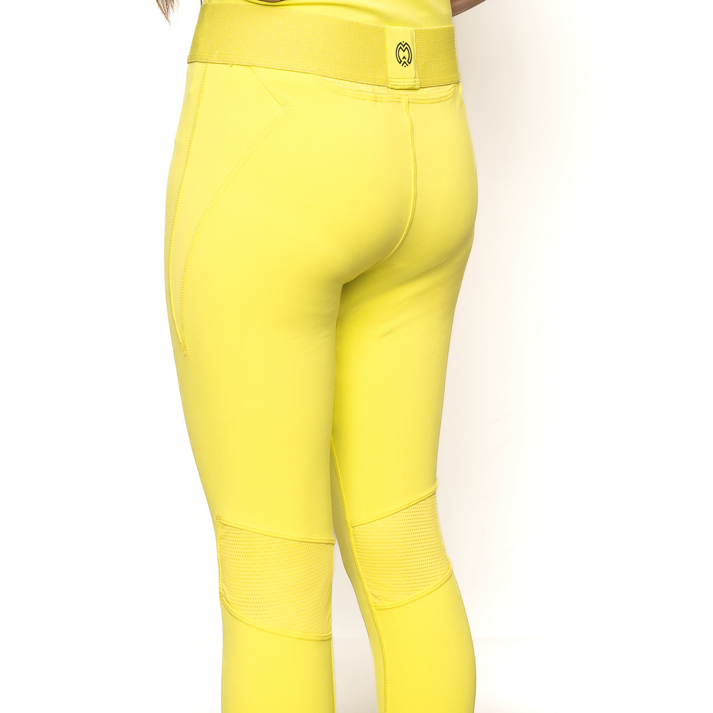 A person is shown from the waist down wearing bright yellow Massov ProForm® Girls’ Athletic Leggings, which are fitted with textured knee panels and a logo patch on the back waistband, set against a plain white background.