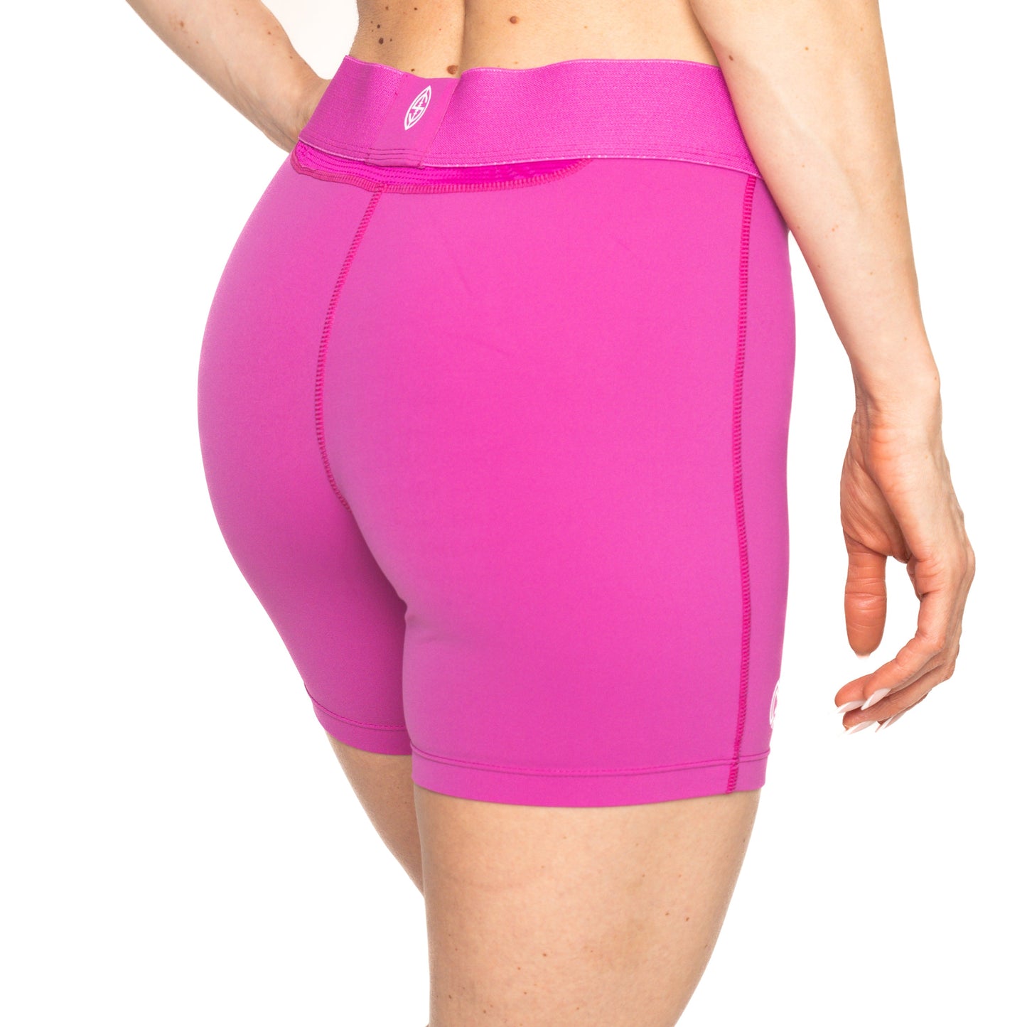 A person stands with their back to the camera, wearing Massov ProForm® Girls' Mid-Rise 5″ Compression Shorts in bright pink, featuring visible seams, a wide logo waistband, and fitted design against a plain white background.