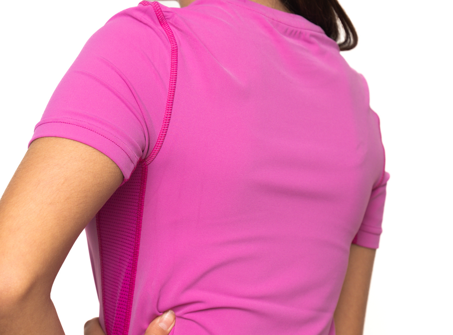 A girl is shown from the back wearing a Massov ProForm® Girls' Short Sleeve Compression Shirt in bright pink. Her left hand rests on her lower back, and her head is turned slightly right. Only her upper body is visible against a white background.