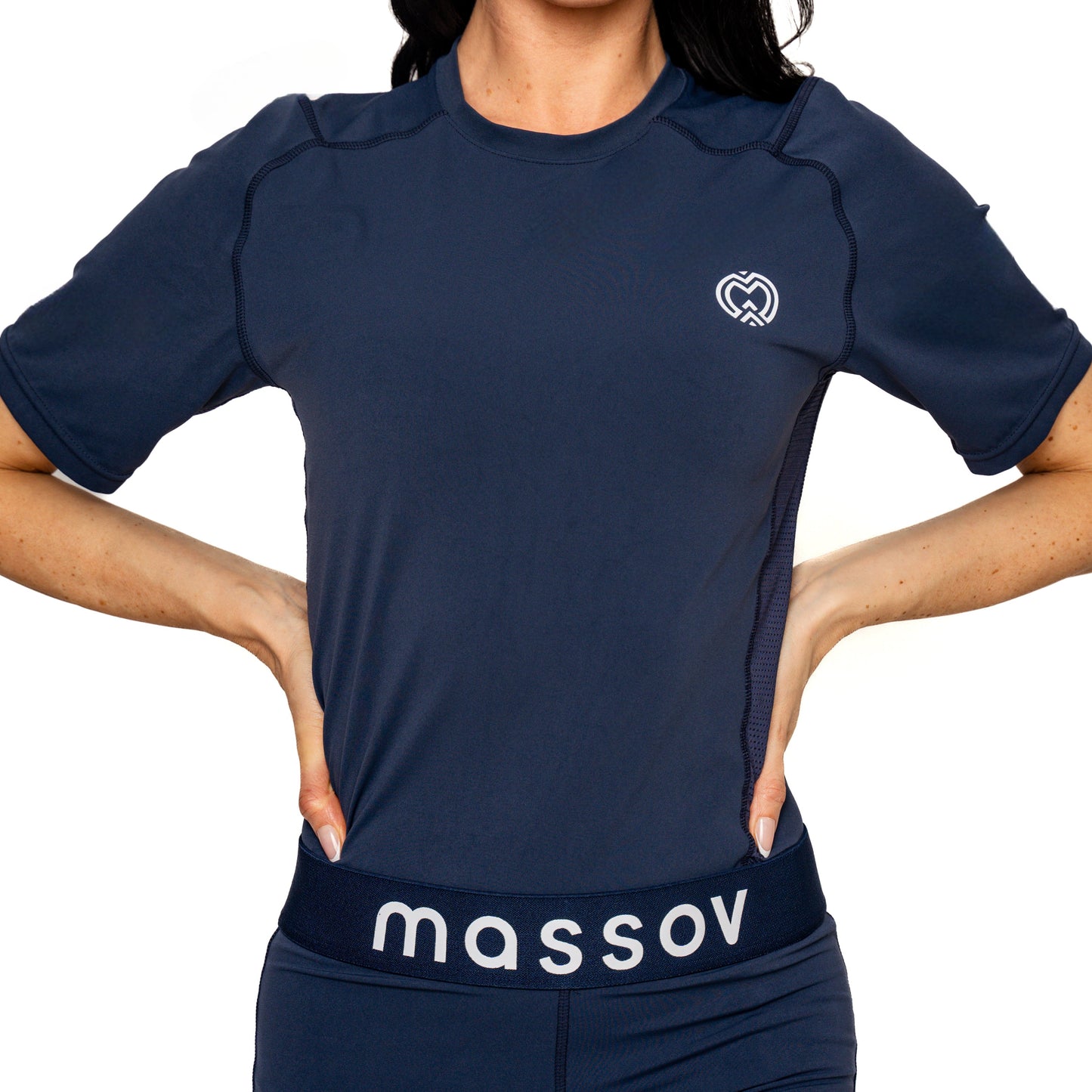 A girl stands hands-on-hips in a navy ProForm® Girls' Short Sleeve Compression Shirt by Massov, with a small heart logo and matching leggings featuring "massov" in white on the waistband, set against a plain white background.