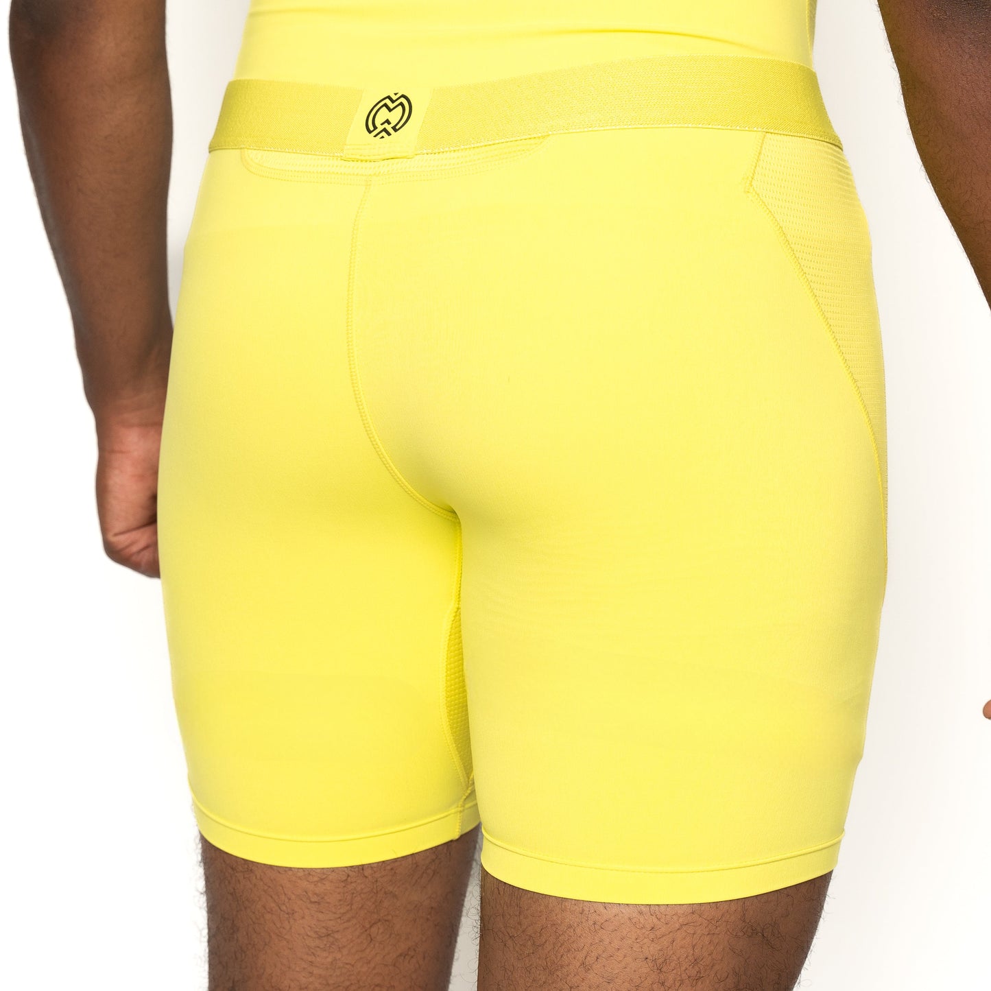A person is shown from the waist down, wearing Massov ProForm® Men’s 7″ Compression Shorts in bright yellow with a subtle waistband logo. The high-performance compression design stands out against a plain white background.
