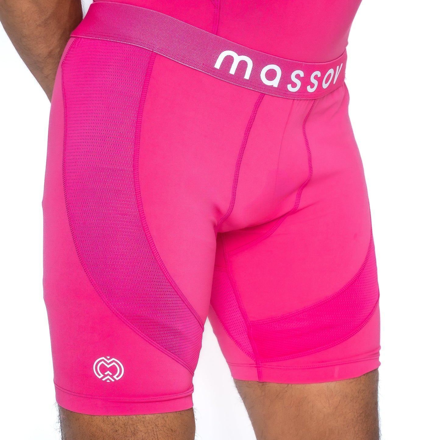 A person wears Massov ProForm® Men’s 7″ Compression Shorts in bright pink, featuring a wide “massov” waistband, mesh-like panels, and a small white interlocking hearts logo on the left thigh.