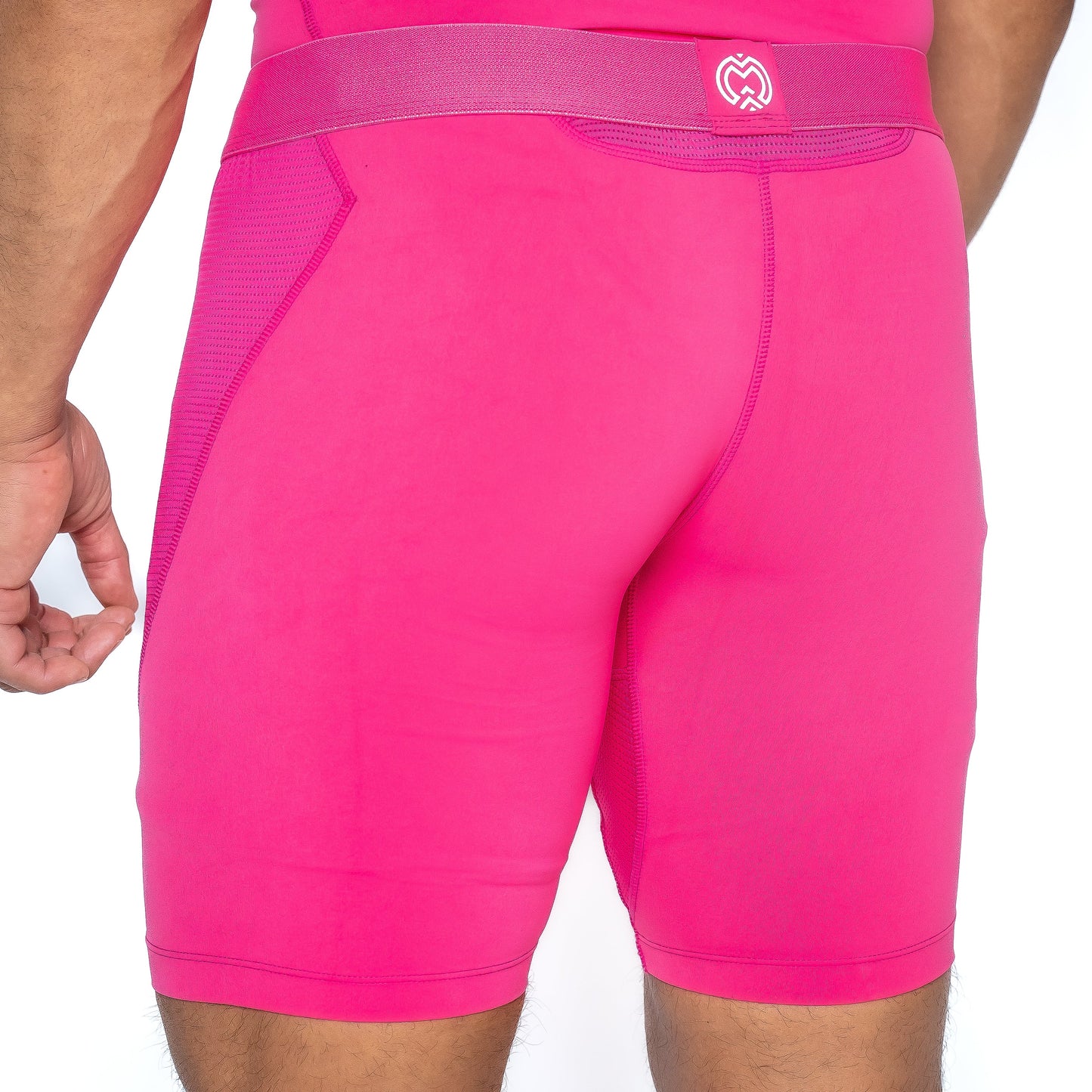 A person wearing Massov ProForm® Men’s 7″ Compression Shorts in bright pink is shown from the back waist to mid-thigh. Features include a textured side panel, wide waistband with a white heart logo, and reinforced stitching. Part of the left arm is visible.