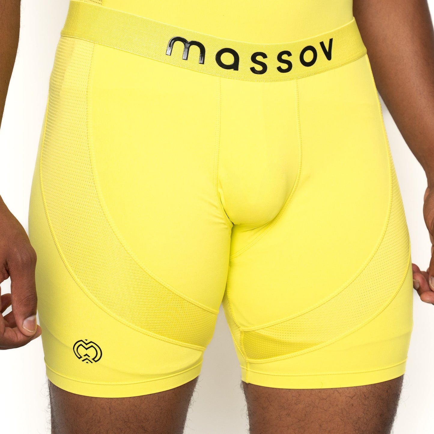 A person wears Massov ProForm® Men’s 7″ Compression Shorts in bright yellow with a black logo on the left thigh, mesh panels, and "massov" in black on the waistband. Hands are at their sides.