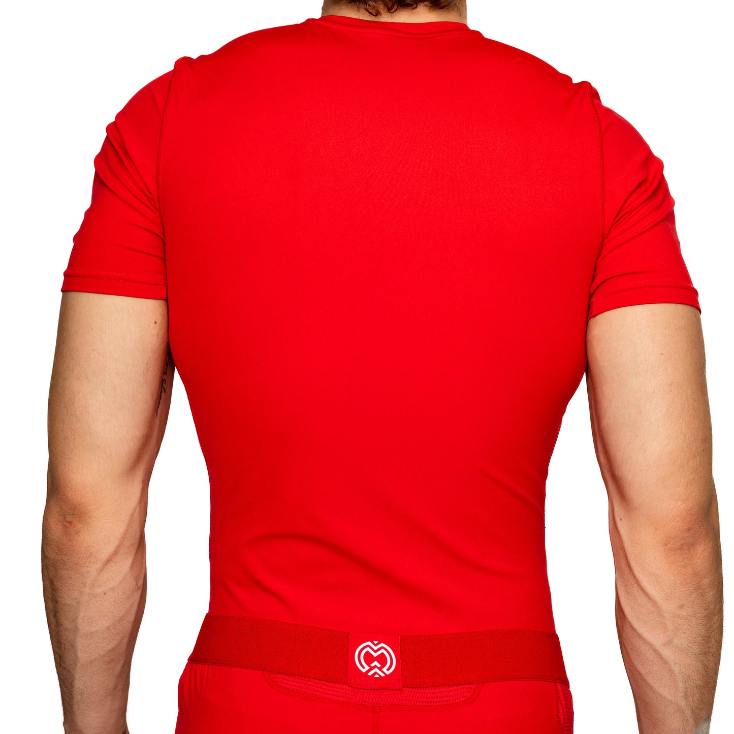 A person with light skin and short brown hair is seen from the back wearing the Massov ProForm® Men’s Short Sleeve Compression Shirt in red, featuring a fitted, moisture-wicking design and a red waistband with a small white logo. The background is white.