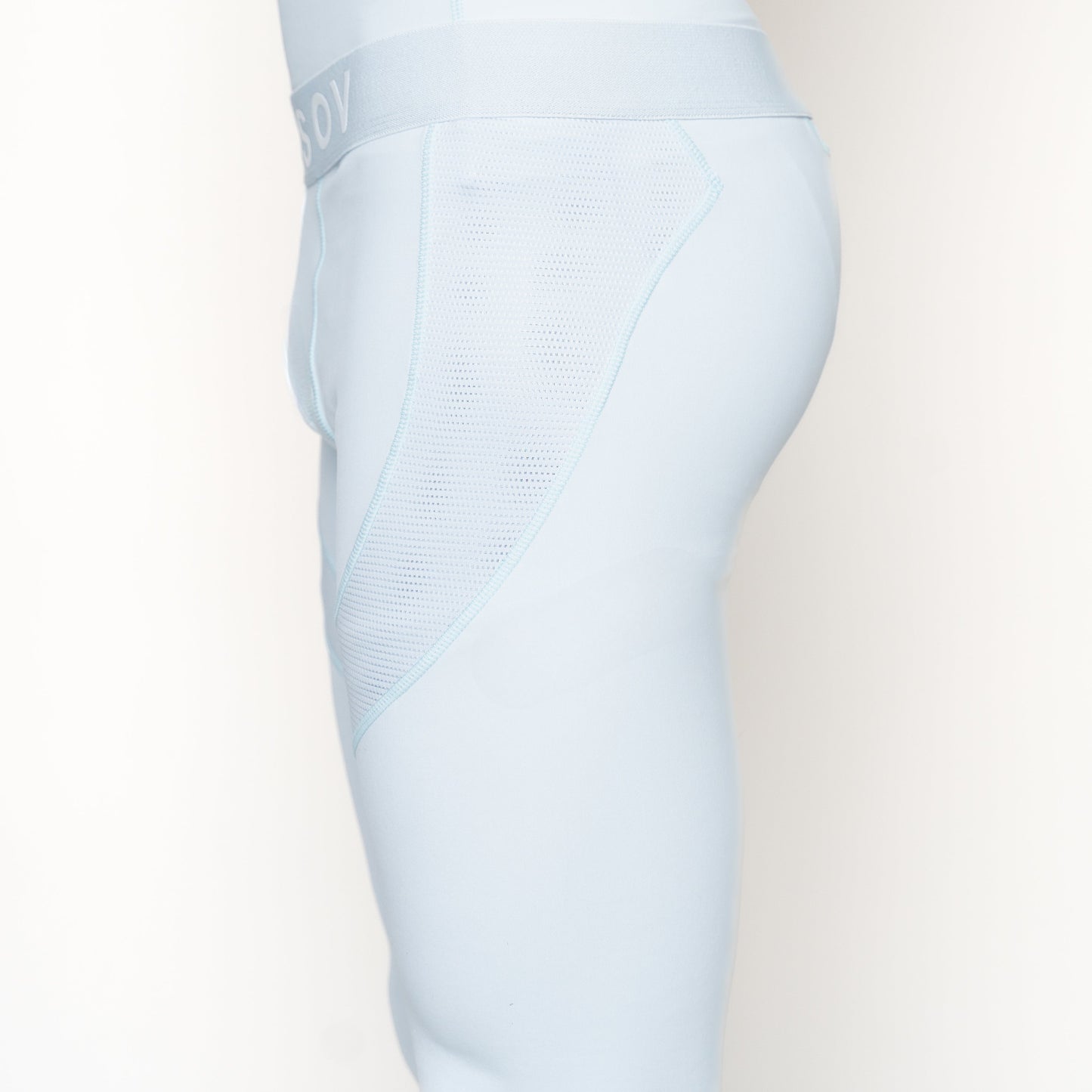 Side view of a person wearing Massov ProForm® Men's Compression Pants in light blue, featuring a wide waistband and mesh panels on the hip and thigh. Only the lower torso and upper leg are visible against a plain white background.