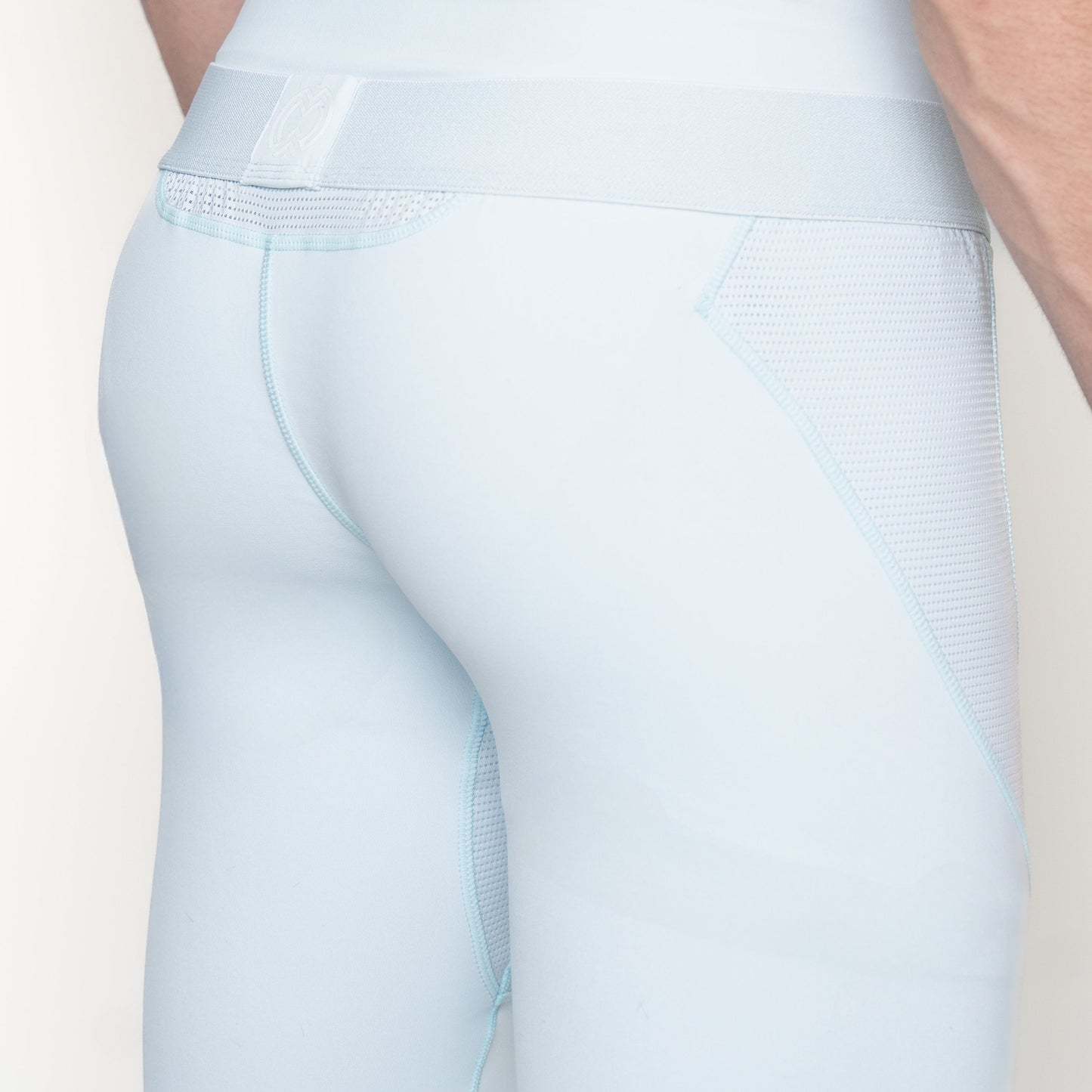 Close-up of a person’s lower back and upper thighs wearing Massov ProForm® Men's Compression Pants in light blue, featuring mesh side panels, a wide waistband, and well-lit, moisture-wicking fabric that highlights the texture and seams.