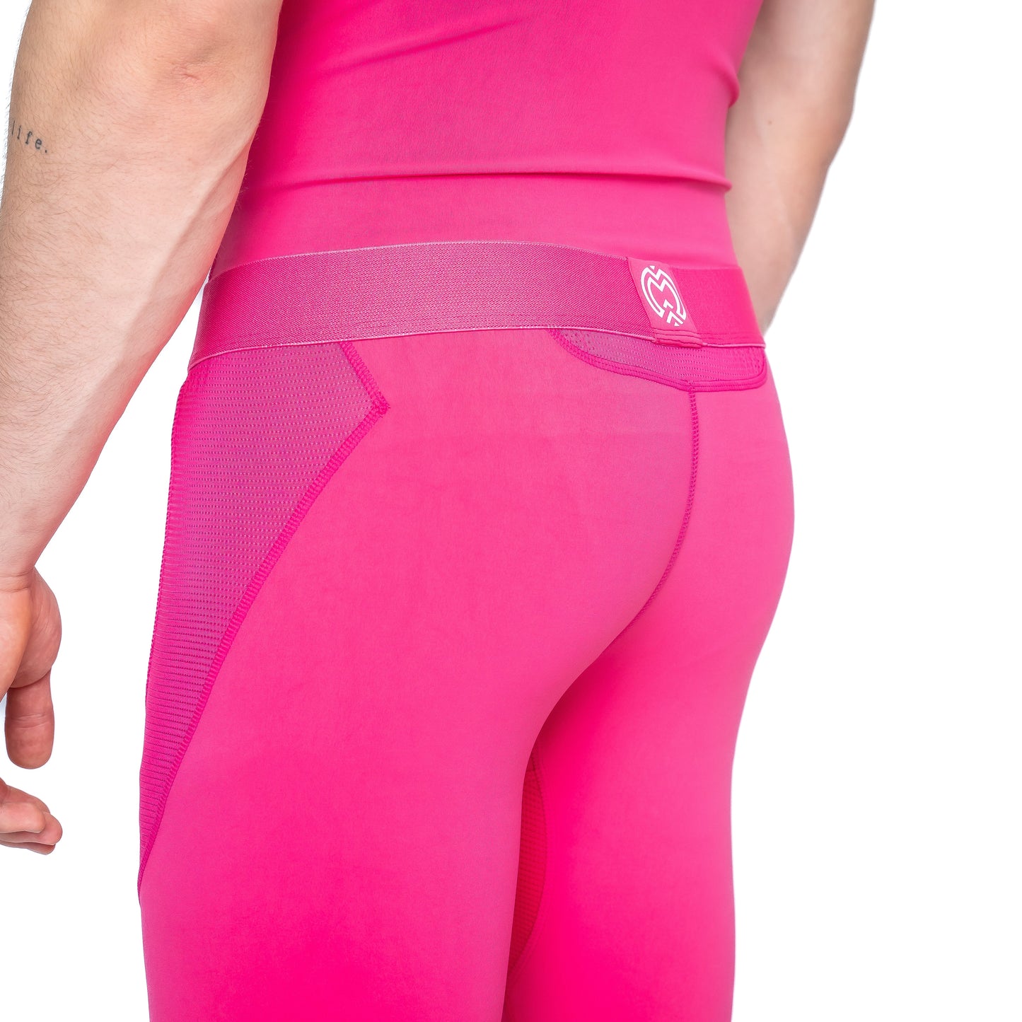A person is seen from the back wearing Massov ProForm® Men's Compression Pants in bright pink, featuring a wide waistband, mesh side panels, and moisture-wicking fabric. A small forearm tattoo is visible.
