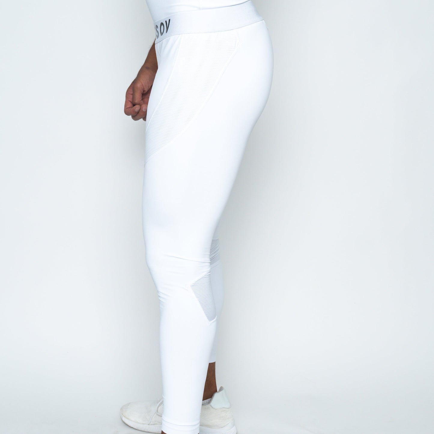 A man stands sideways against a white background, showing only his lower torso and legs. He wears Massov ProForm® Men's Compression Pants with a subtle textured pattern near the thigh and calf, paired with white sneakers.