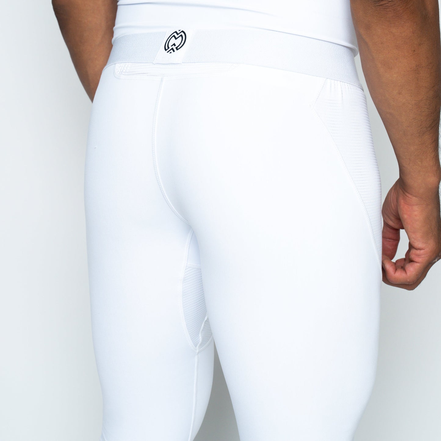 A person wearing Massov ProForm® Men's Compression Pants is shown from the back, emphasizing the waist and legs. The waistband has a small black and white logo at the center, with the right hand resting by their side against a white background.