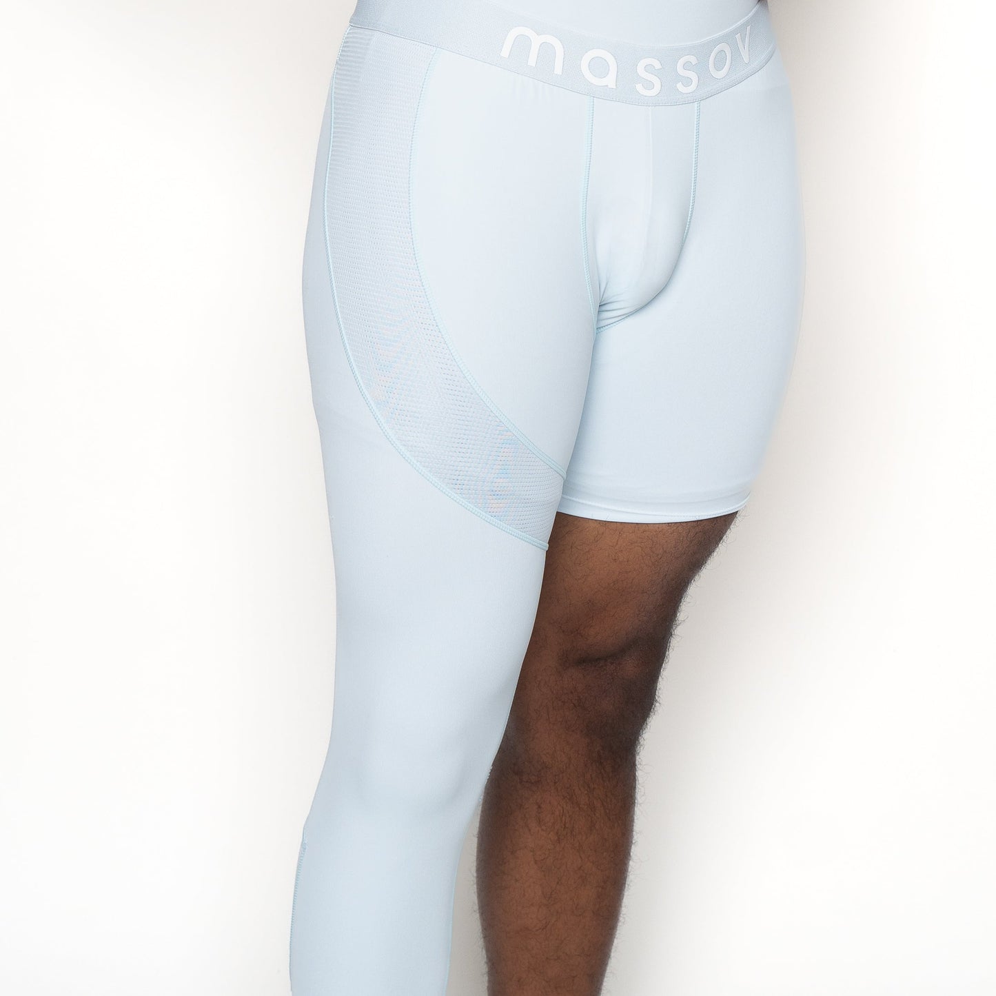 A model wears Massov ProForm® Men's One Leg Compression Pants—light blue, asymmetrical athletic tights with one short and one full-length leg. The waistband reads "massov." Only the midsection and upper legs are shown against a white background.