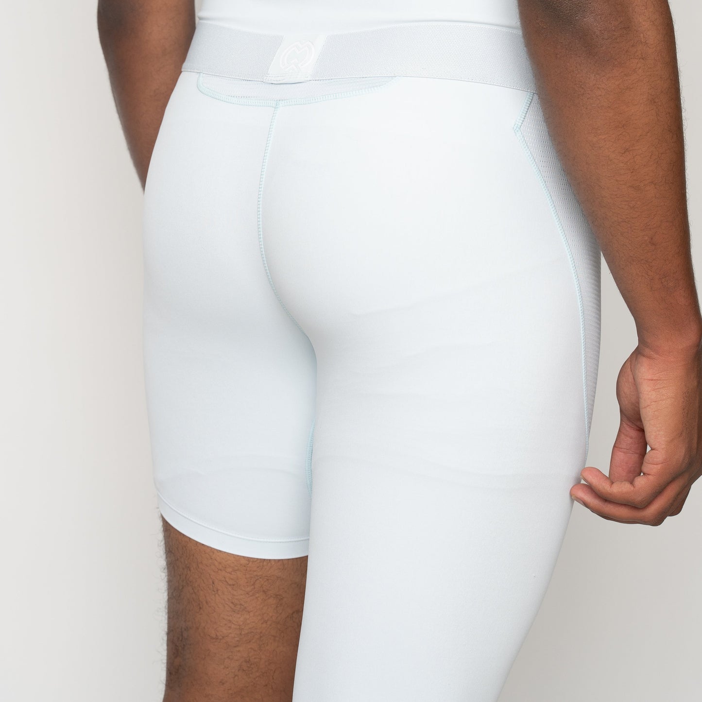 A person stands with their back to the camera, highlighting Massov ProForm® Men's One Leg Compression Pants in light blue. The fitted design and plain background draw attention to the garment and lower body.