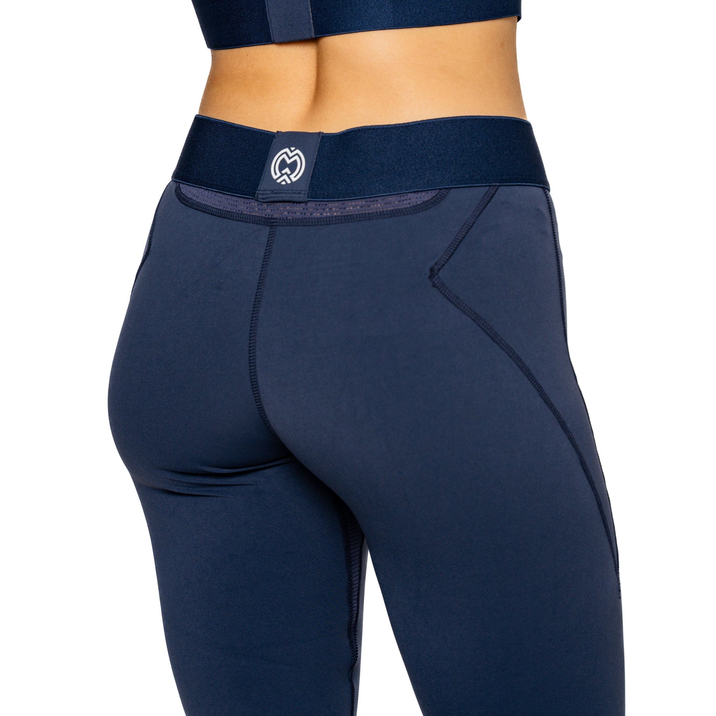 A person wears high-waisted, navy blue Massov ProForm® Women's Compression Leggings with a wide waistband and a small white heart logo on the back. A matching sports bra is partially visible against a plain white background.