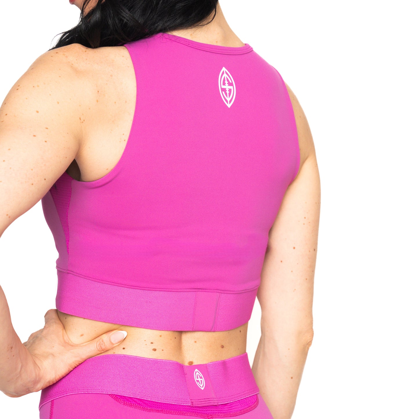 A person stands with their back to the camera, wearing a pink Massov ProForm® Women's Longline Sports Bra with moisture-wicking fabric and a small white logo on the upper back. One hand rests on their hip against a white background.