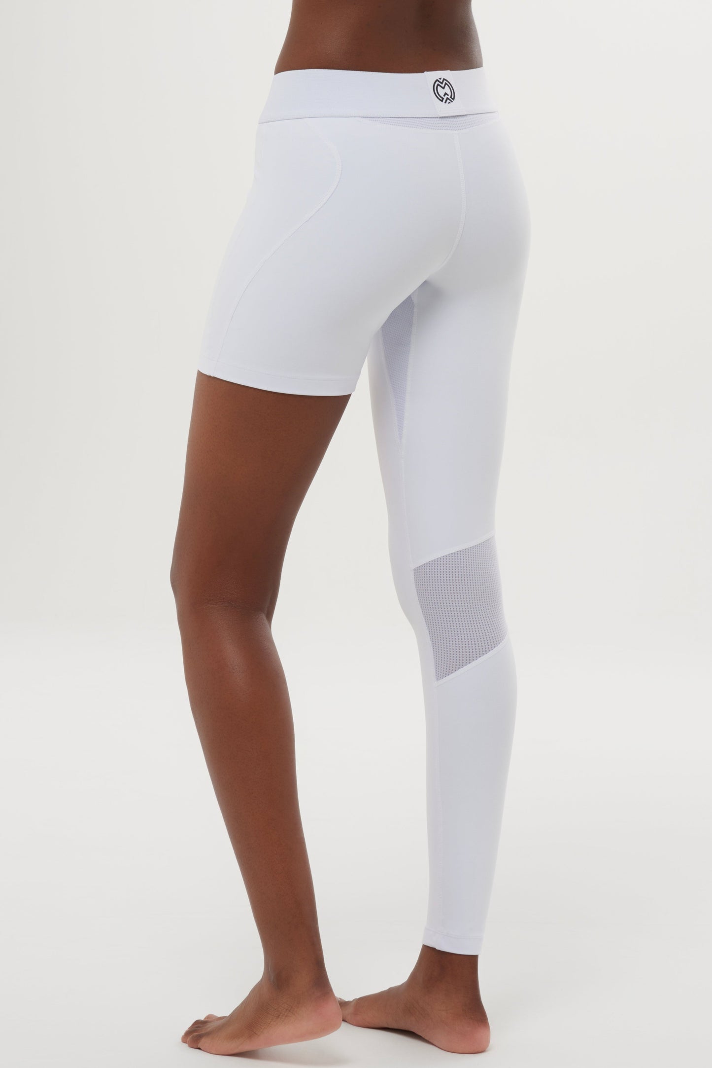A person stands barefoot on a white surface, wearing Massov ProForm® Women's One Leg Compression Pants—featuring an asymmetrical design with one fitted short and one full-length compression legging with mesh. The background is plain white.