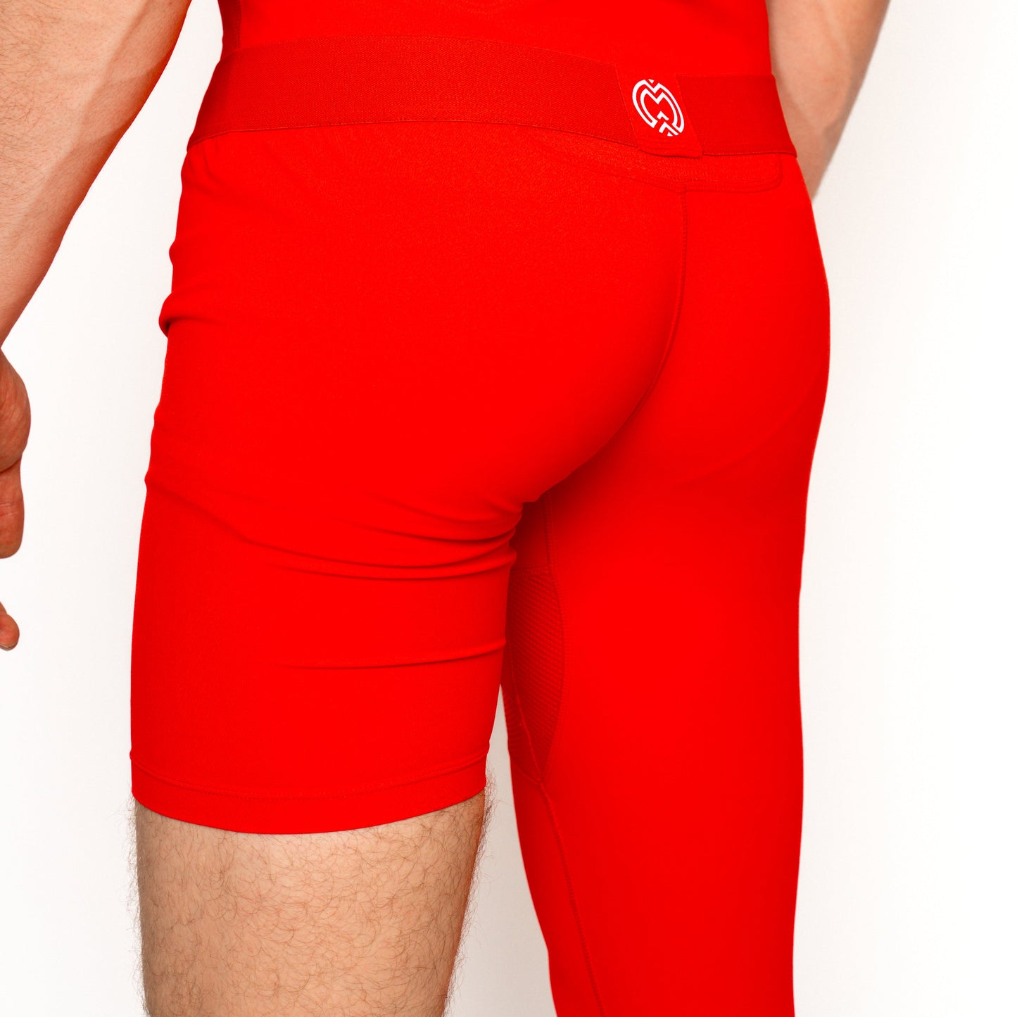 A youth is shown from the back and left side, wearing Massov ProForm® Youth Boys' One Leg Compression Pants in bright red. A small white heart logo appears on the waistband, set against a plain white background.