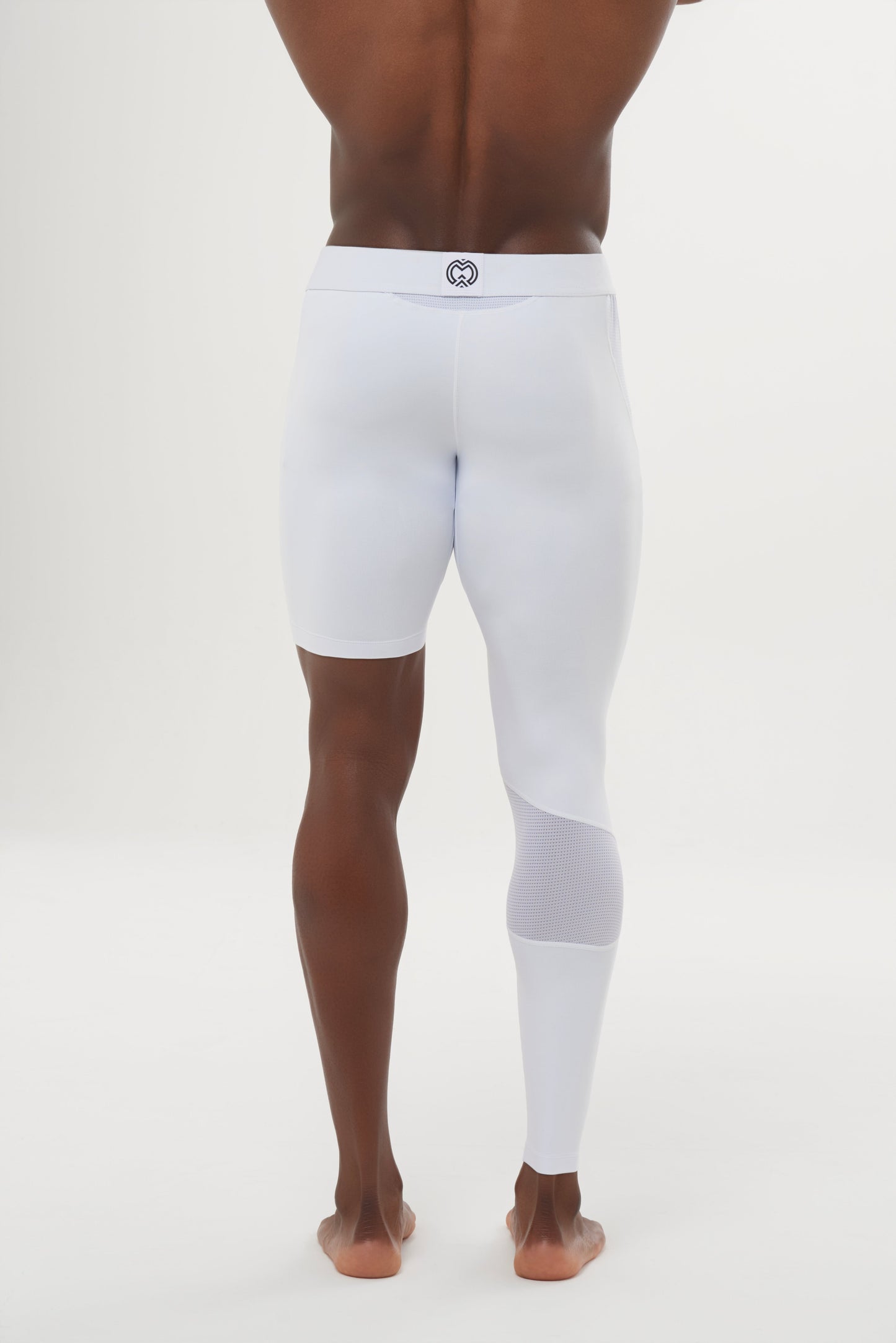 A person stands barefoot, facing away, wearing Massov ProForm® Youth Boys' One Leg Compression Pants—white athletic tights with one leg as shorts and the other full-length. A small circular logo is at the waistband's center against a plain white background.
