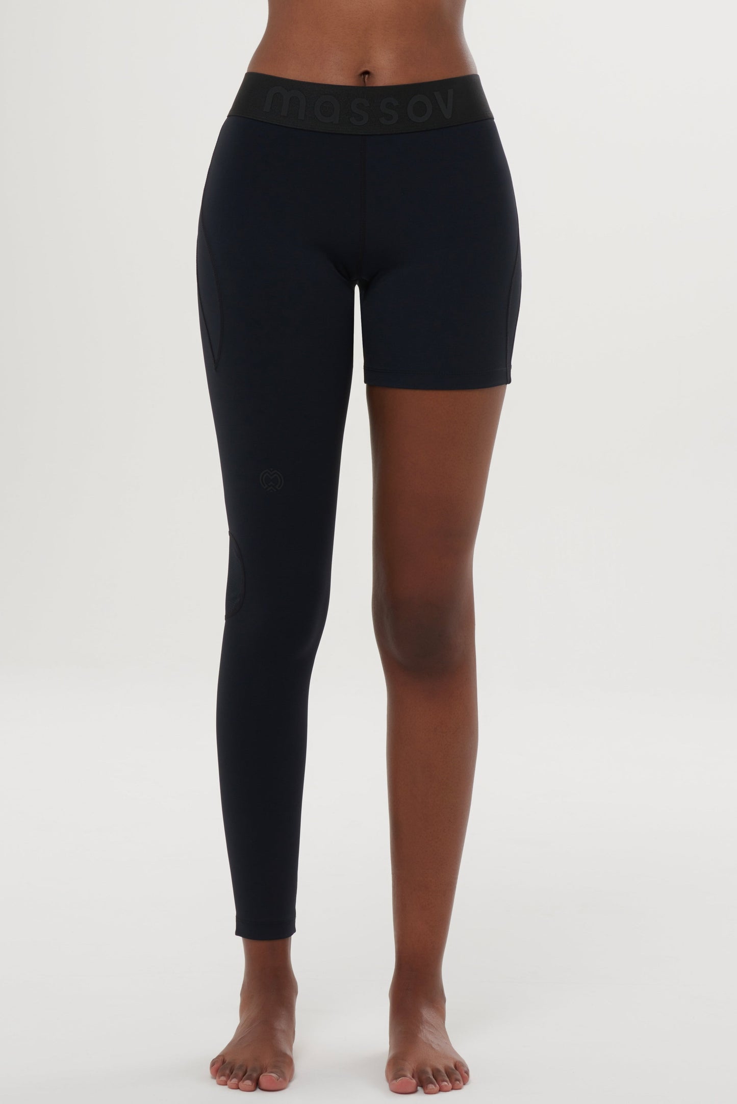 A person stands barefoot against a white background, wearing Massov ProForm® Youth Girls' One Leg Compression Pants: the left leg is full-length, the right is shorts length. The thick waistband subtly features the brand name. The upper body isn't visible.