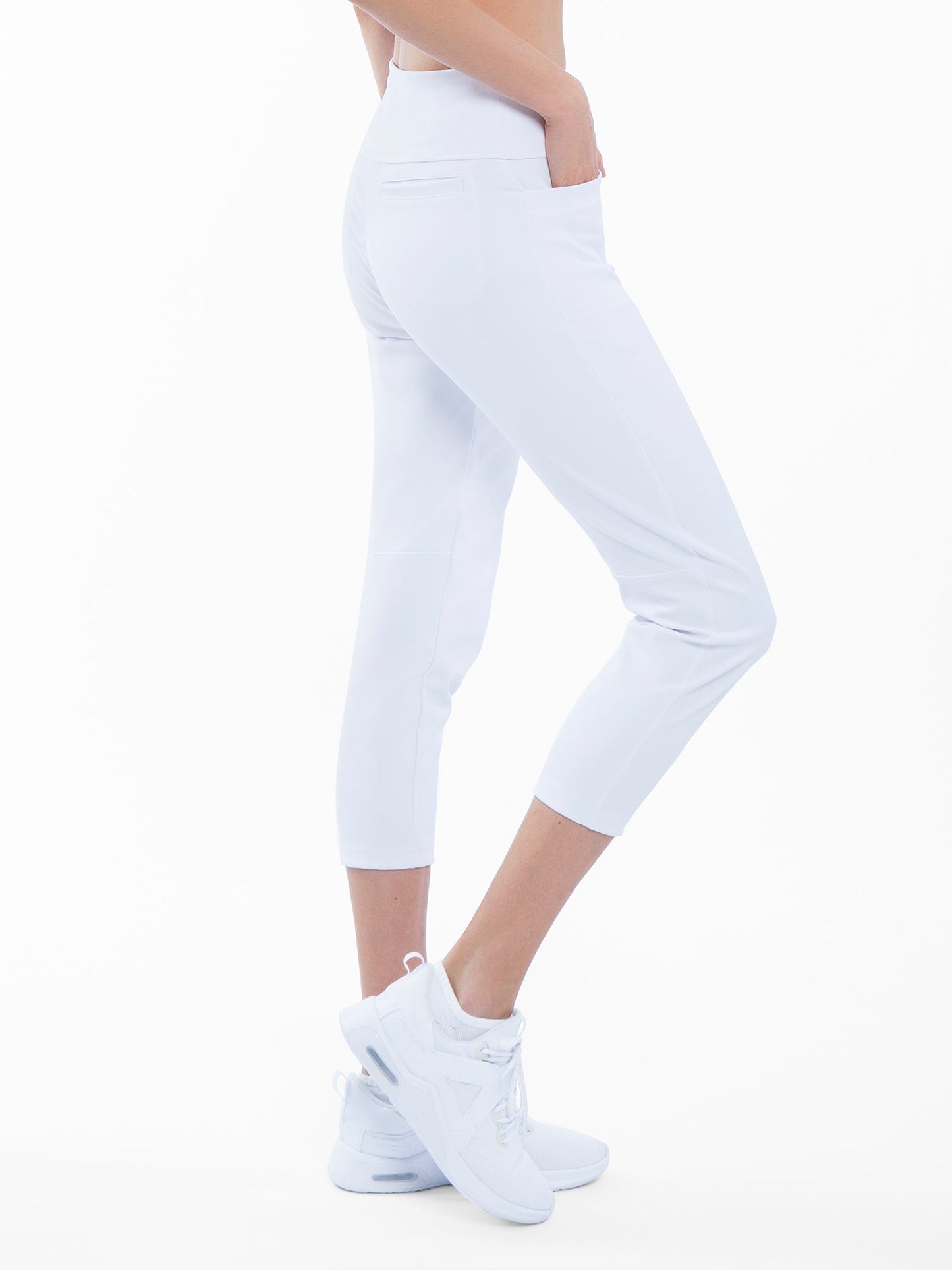 A person stands in profile, wearing inPhorm NYC Quick Dry Women's Golf 24" Capri - White with UPF 50+ protection and white shoes. Set against a plain background, only the lower body is visible, highlighting clean lines and subtle back pockets.