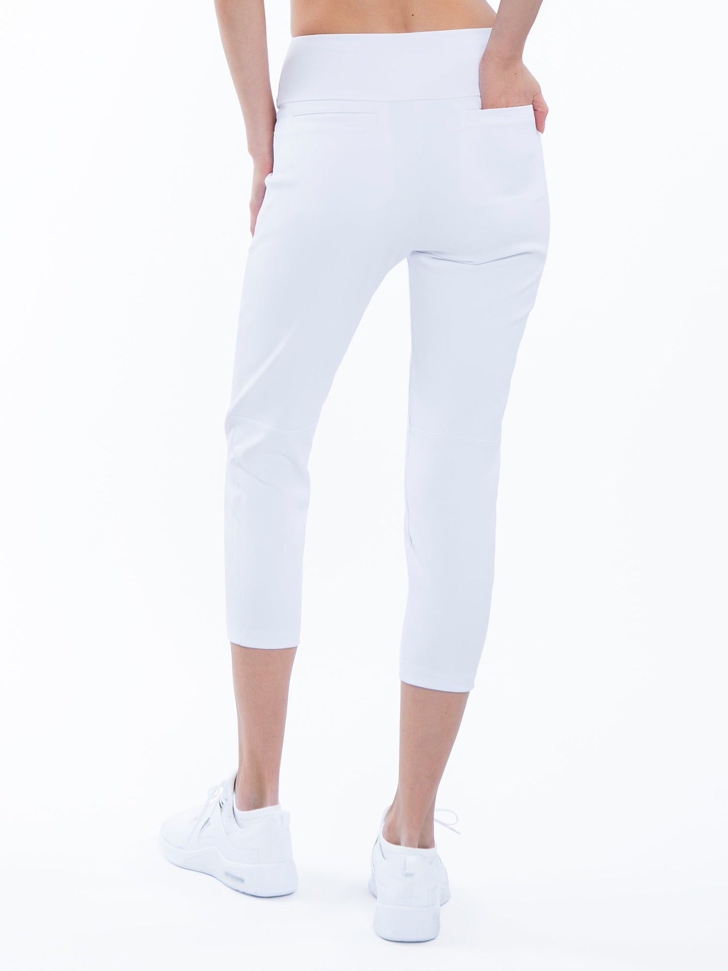 A person faces away wearing inPhorm NYC's Quick Dry Women's Golf 24" Capri in white, featuring UPF 50+ protection, high waist, and a visible back pocket for their right hand. They pair the capris with white sneakers against a plain white background.