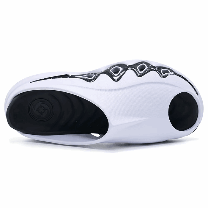 A close-up of the BPBazaar Rigorer Shark 3 Slides 'White/Black' displays black grip sections at the heel and forefoot, wavy midsole accents, and highlights the tread and contours from a bottom view.