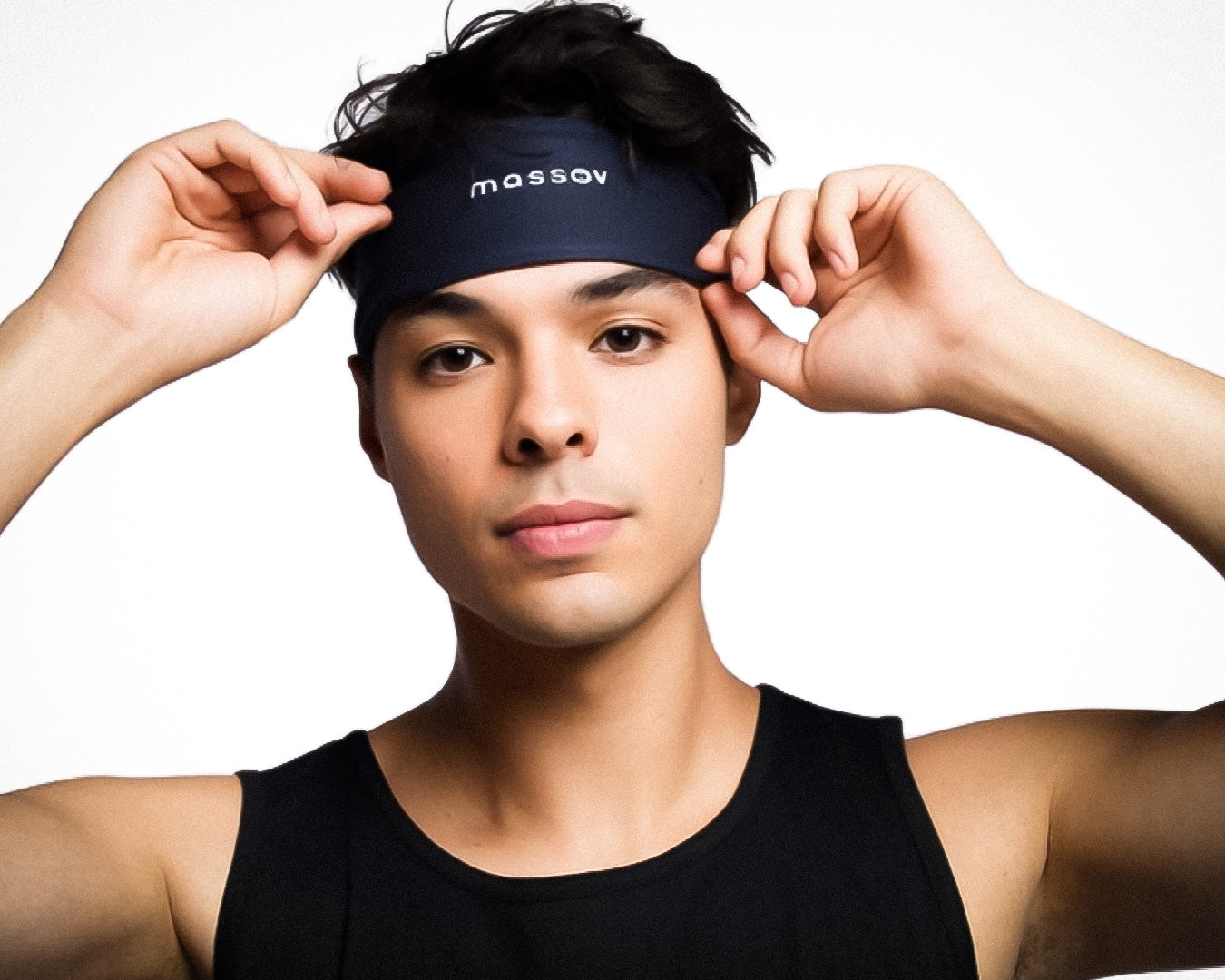 A young person with short dark hair adjusts a black Massov Sports Headband. They wear a black sleeveless top and face the camera against a plain white background.