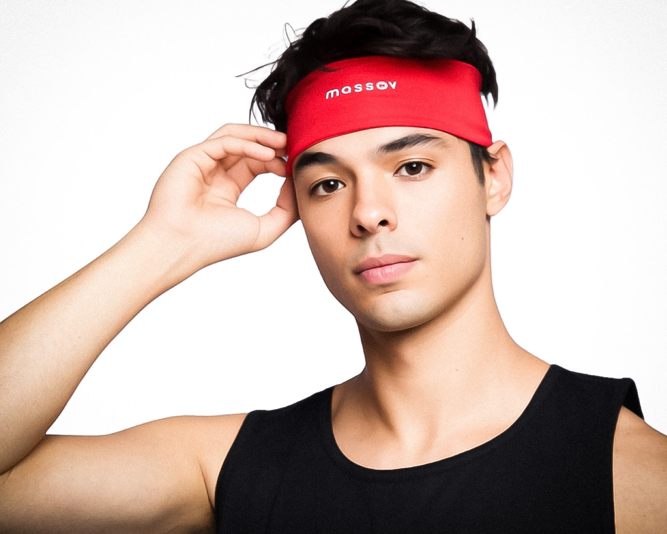 A young man with short dark hair wears the Massov Sports Headband in red and a black tank top, facing forward against a plain white background, gently touching his headband with a neutral expression.