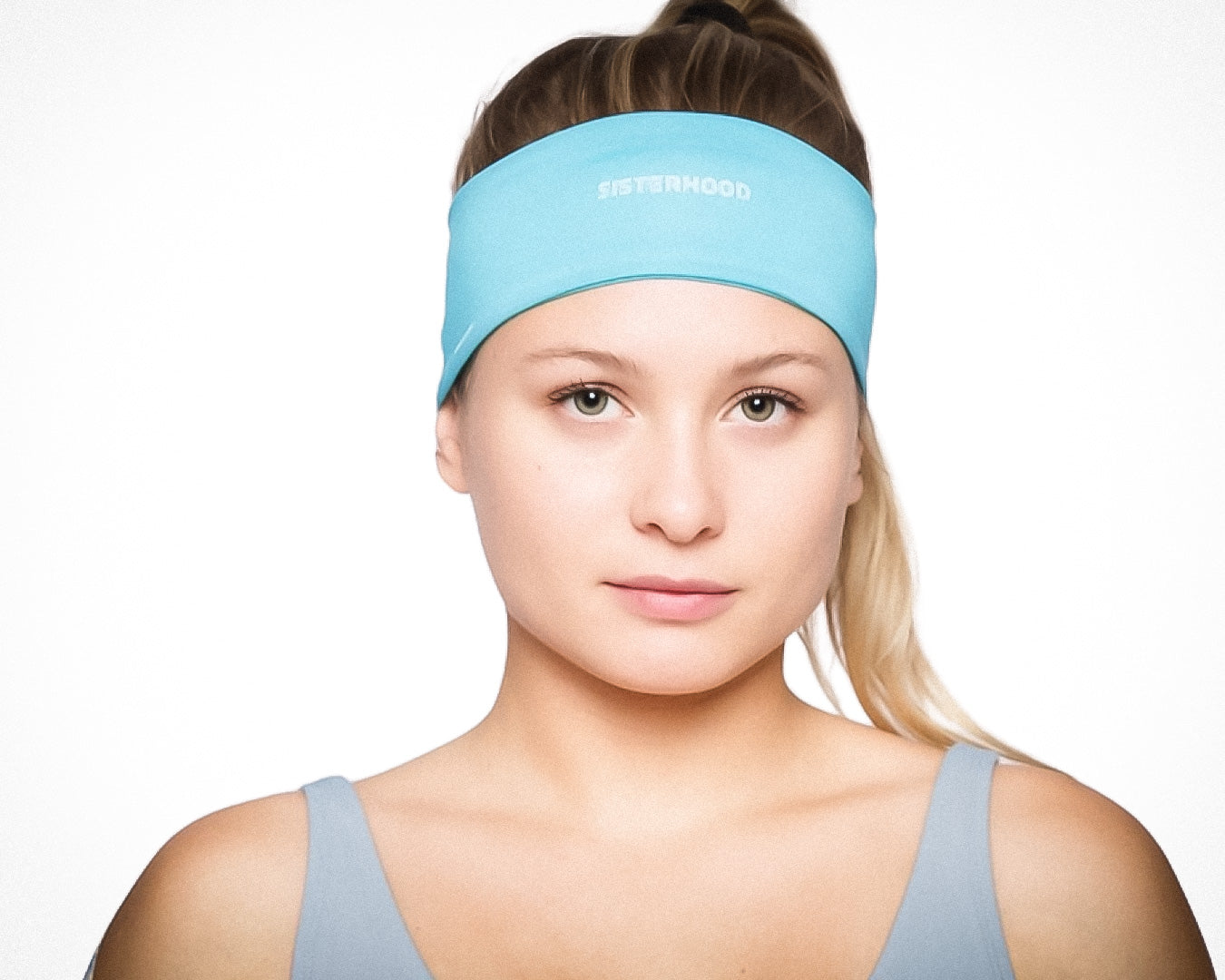 A young woman with fair skin and straight blonde hair pulled back wears a light blue Massov Sports Headband featuring the word "SISTERHOOD," paired with a matching tank top, set against a plain white background.