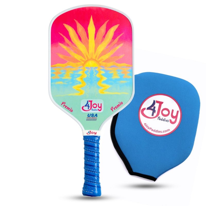 The Sunset 4Joy Pickleball Paddle Premio Series by 4Joy Paddles features a carbon fiber face with a vibrant yellow sun over water on a pink, orange, and blue background, plus a blue grip handle beside a 4Joy paddle cover displaying their logo and website.